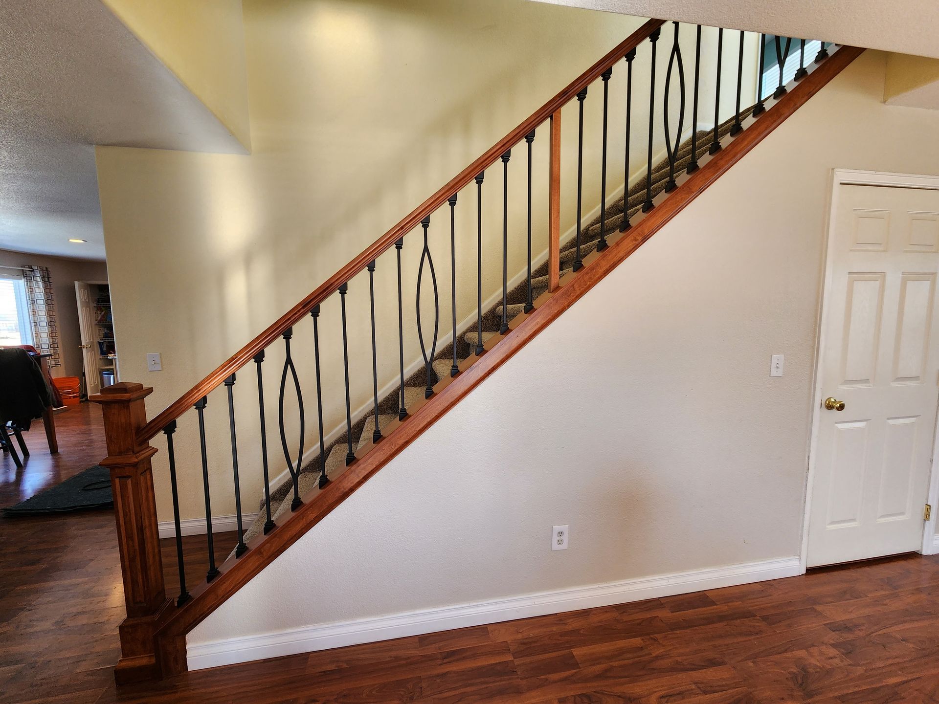 Wooden staircase with black metal spindles and wood railing in a home, next to a white door.