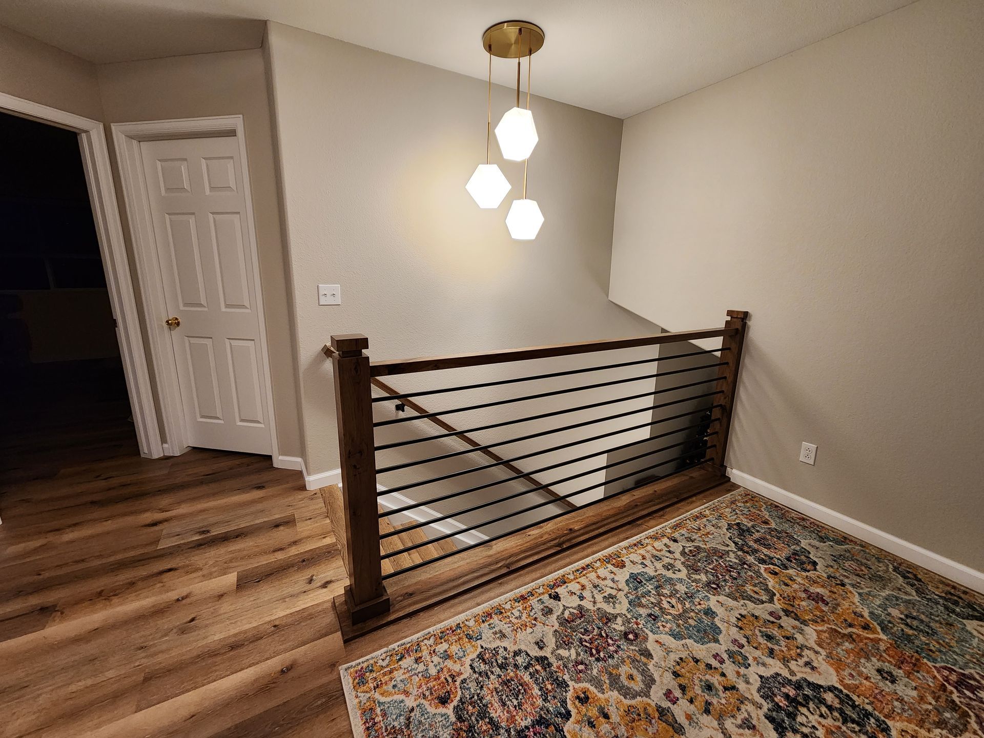 Hallway with hardwood floor, rug, stairs with railing, closed door, and pendant light fixture.