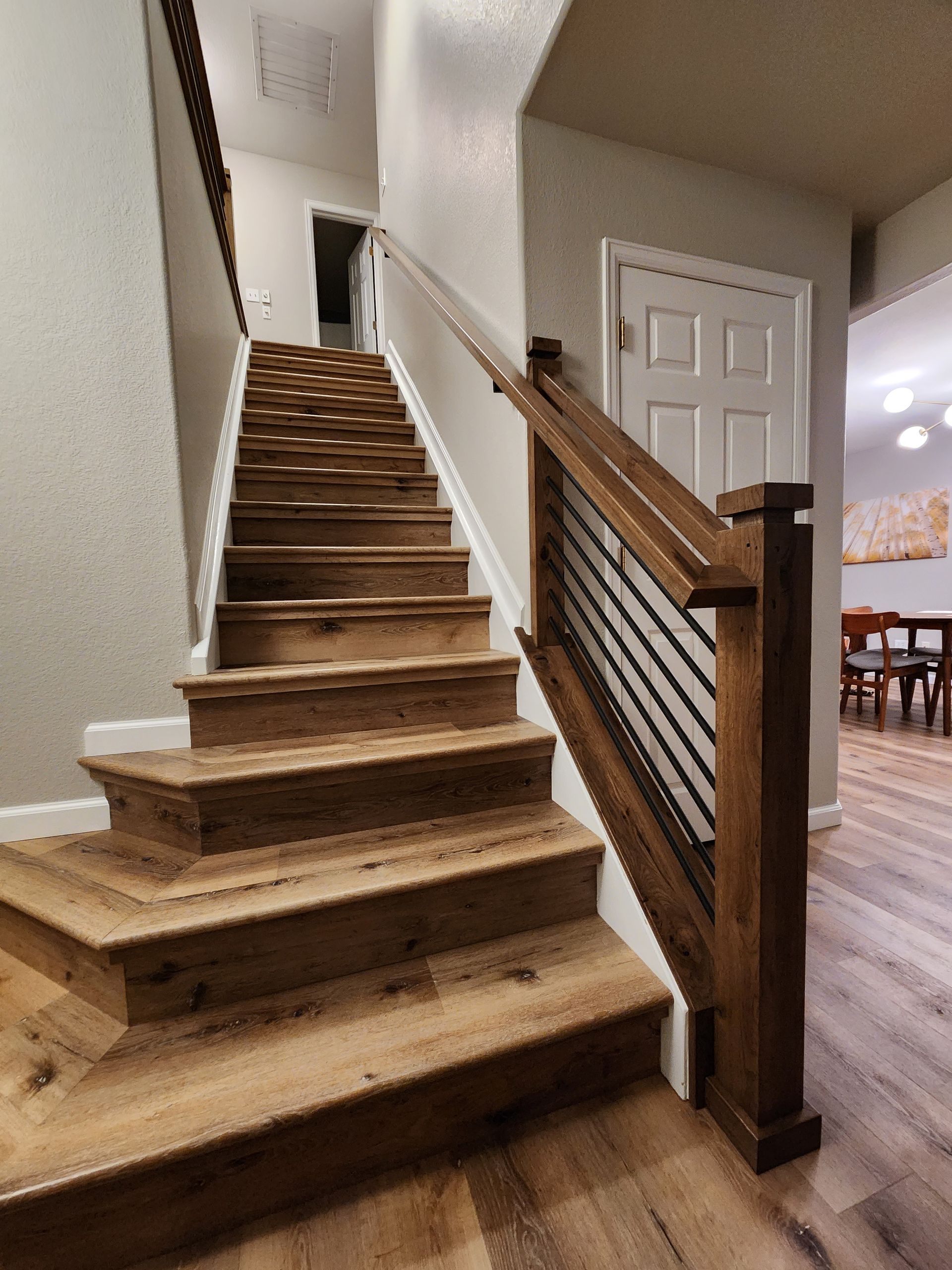 Wooden staircase with metal railing leading to upper floor, neutral walls, and door.