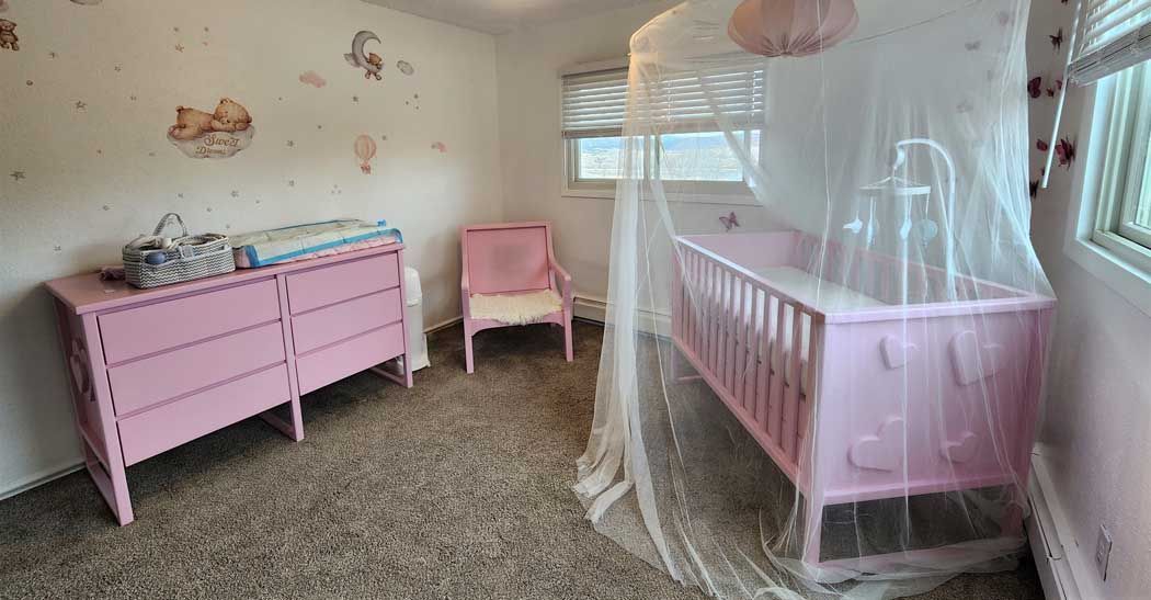 Pink nursery with crib, dresser, and chair; wall art; light coming in from a window.