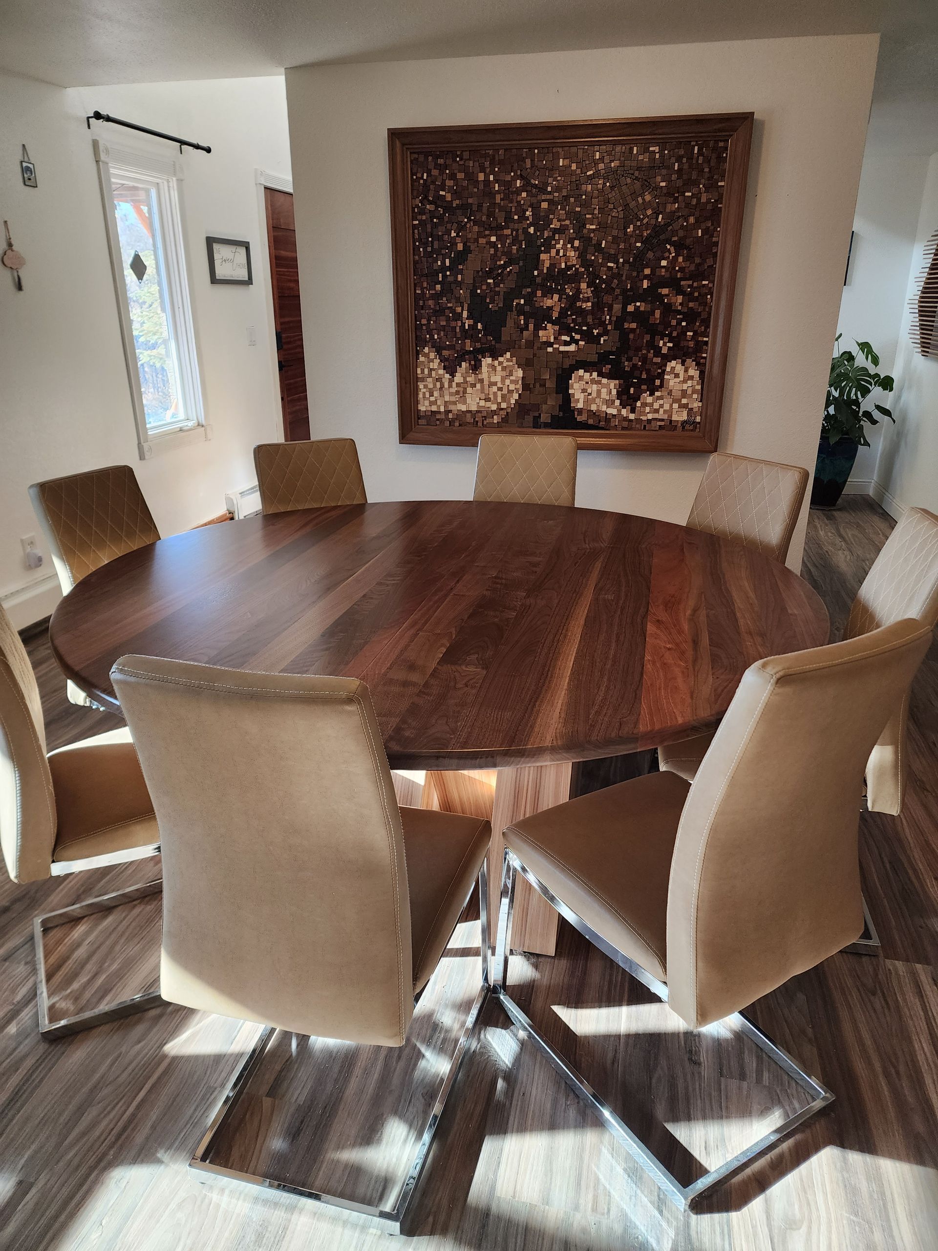 Round wooden dining table with eight beige upholstered chairs in a room with wood flooring.