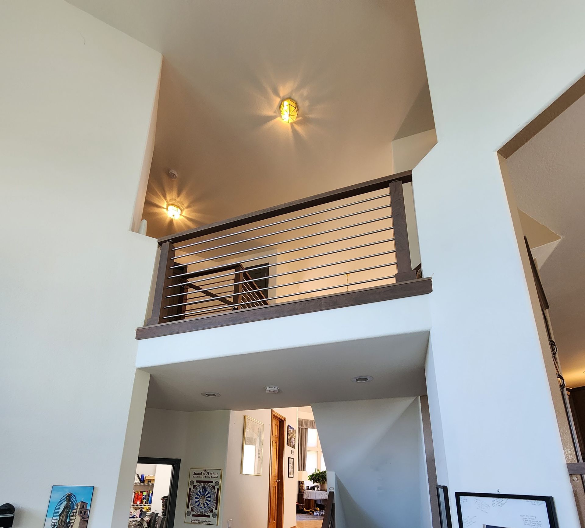 Interior view of a two-story home, showing a staircase, railing, and overhead lighting.