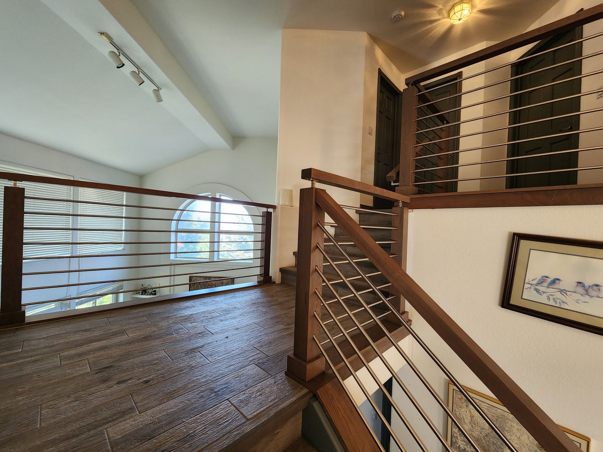 Wooden stairs and railing with metal cables, leading to a second-floor landing with a large window.