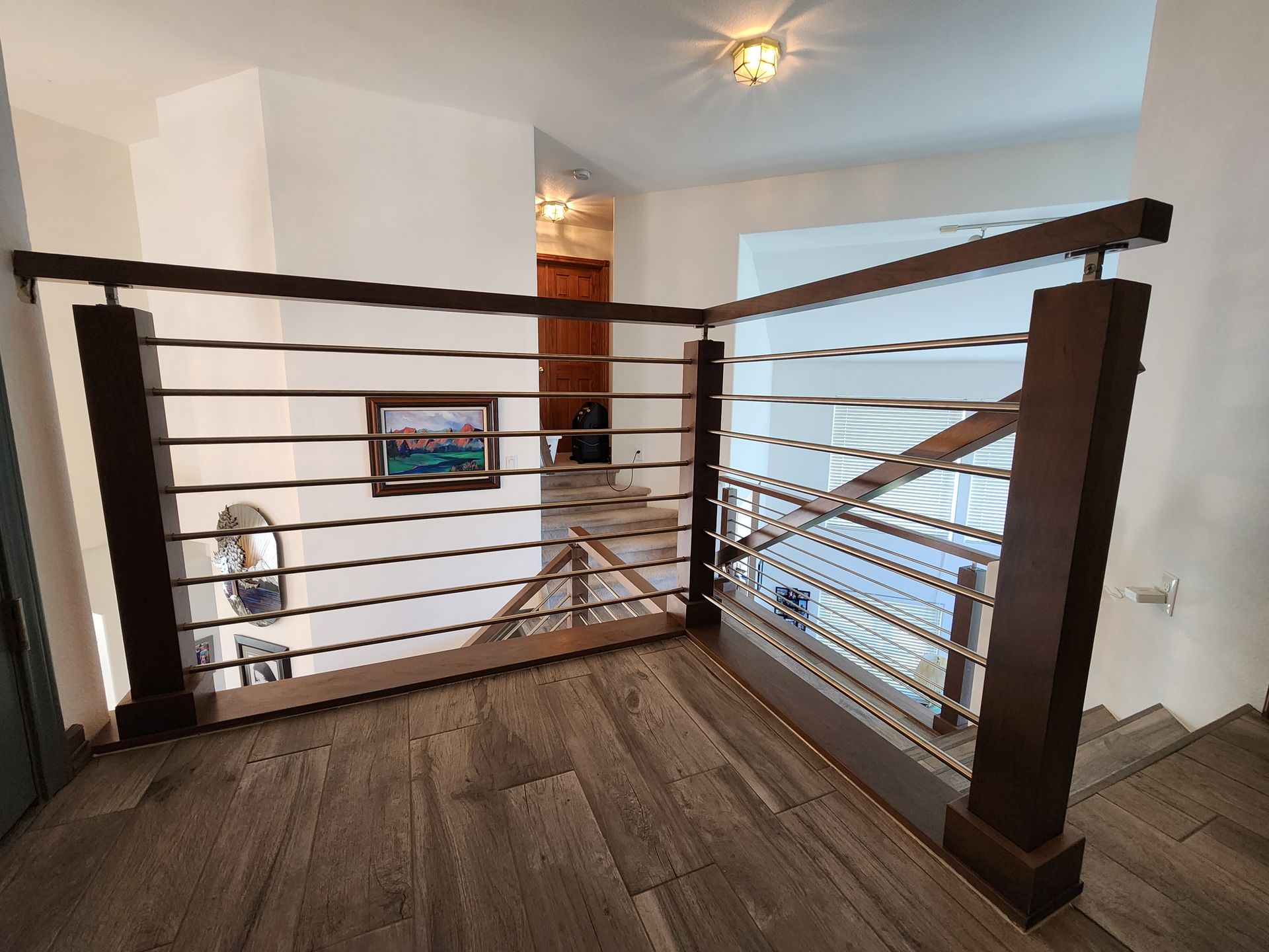 Wooden railing with horizontal metal bars, leading to a staircase in a home.