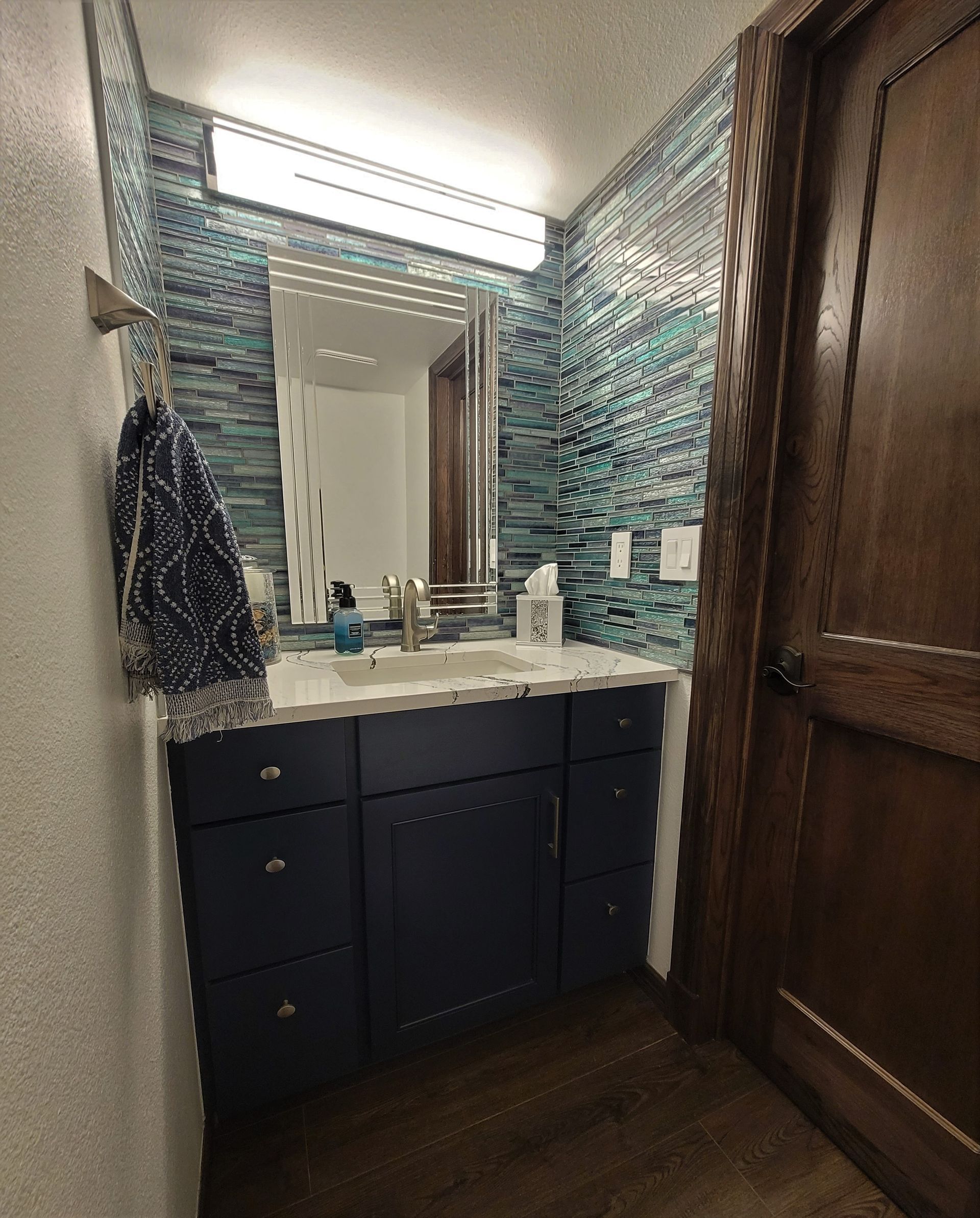 Bathroom with blue vanity, backsplash, mirror, and a wooden door.