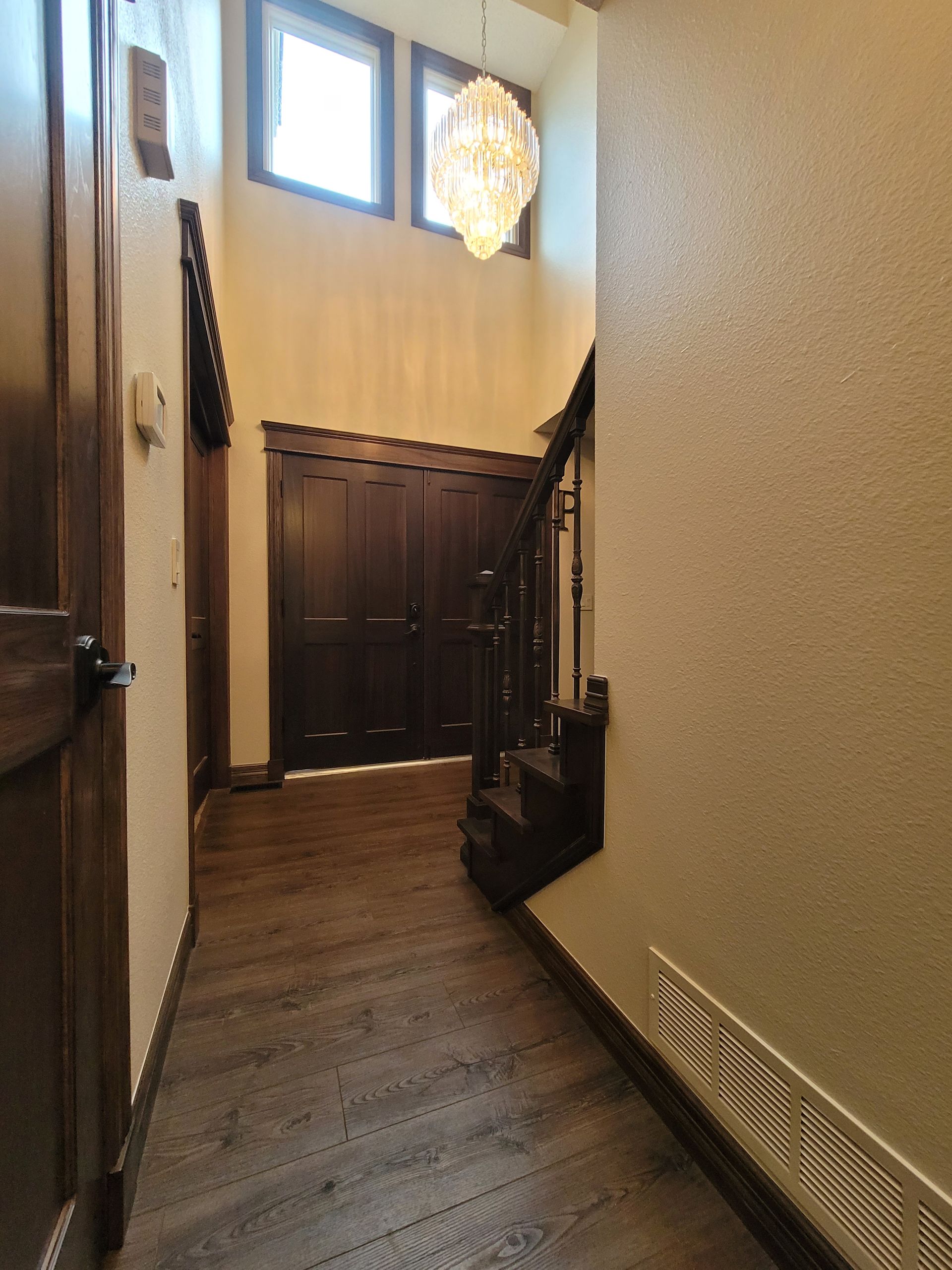 Hallway with wooden floor, stairs, and dark wood doors. A chandelier hangs from the high ceiling.