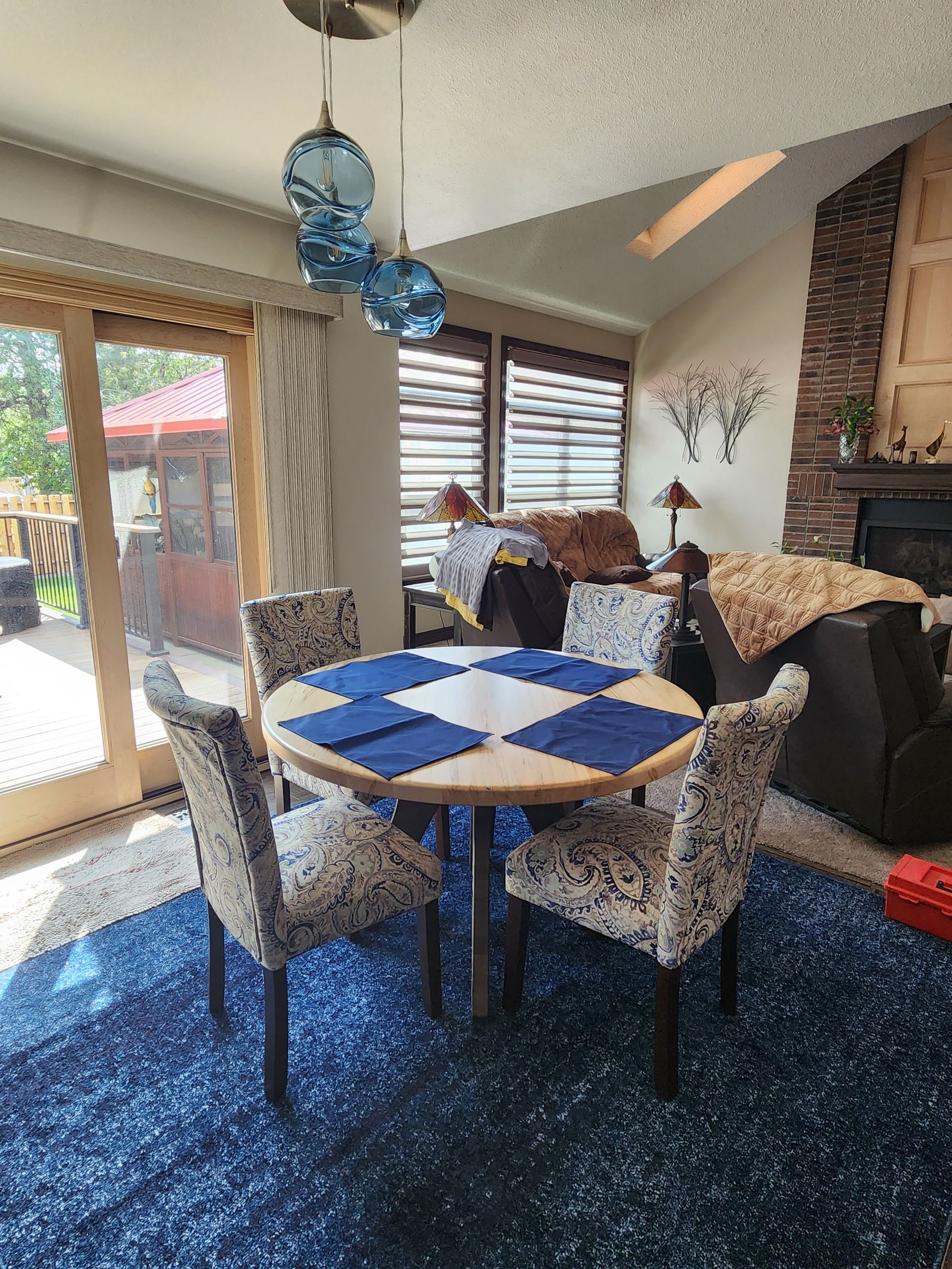 Round dining table with four patterned chairs on a blue rug, next to a sliding door.