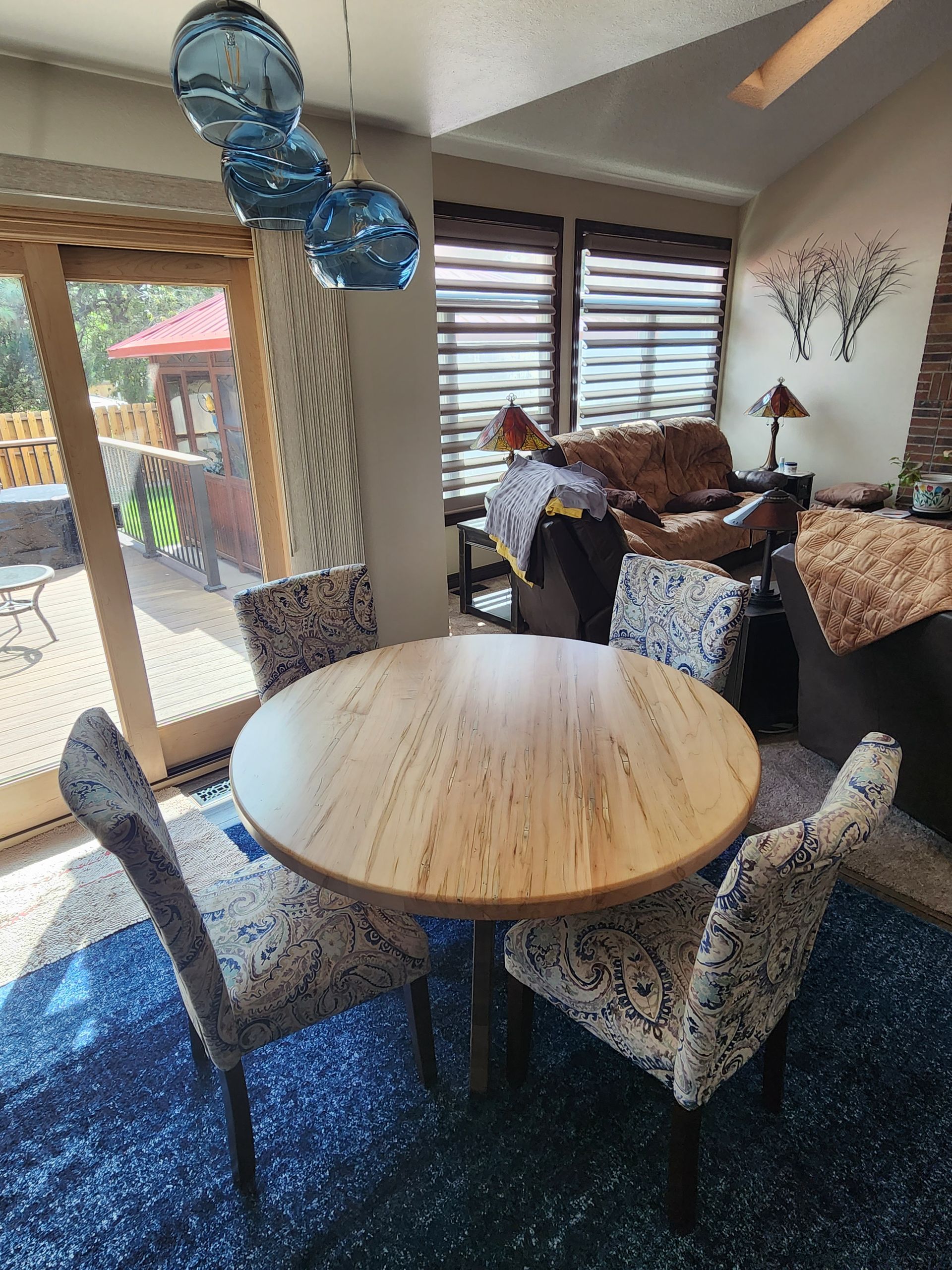 Dining area with round wooden table, four patterned chairs, blue rug, sliding door to patio.