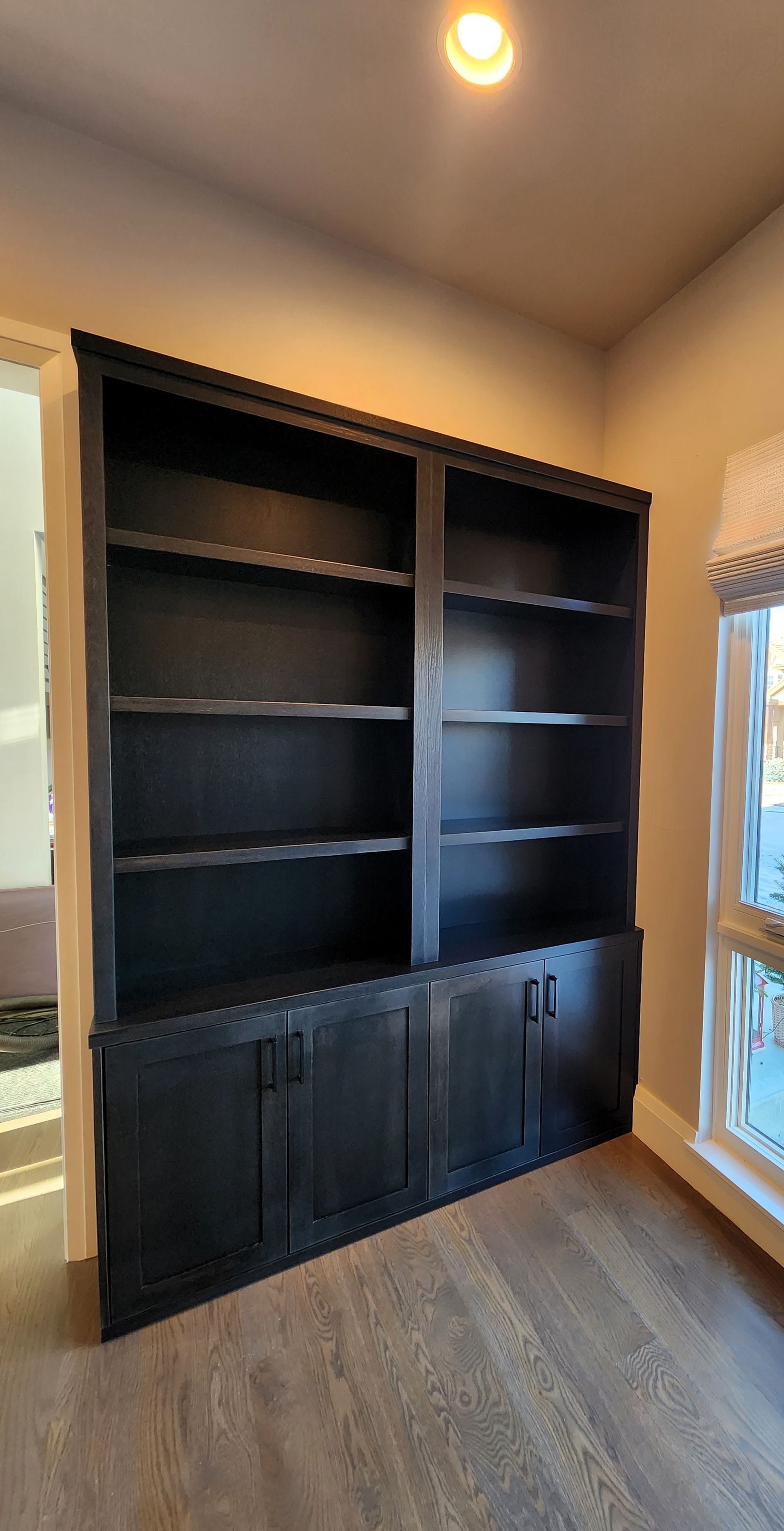 Dark wood built-in bookcase with shelves and lower cabinets in a room with hardwood floors and a window.