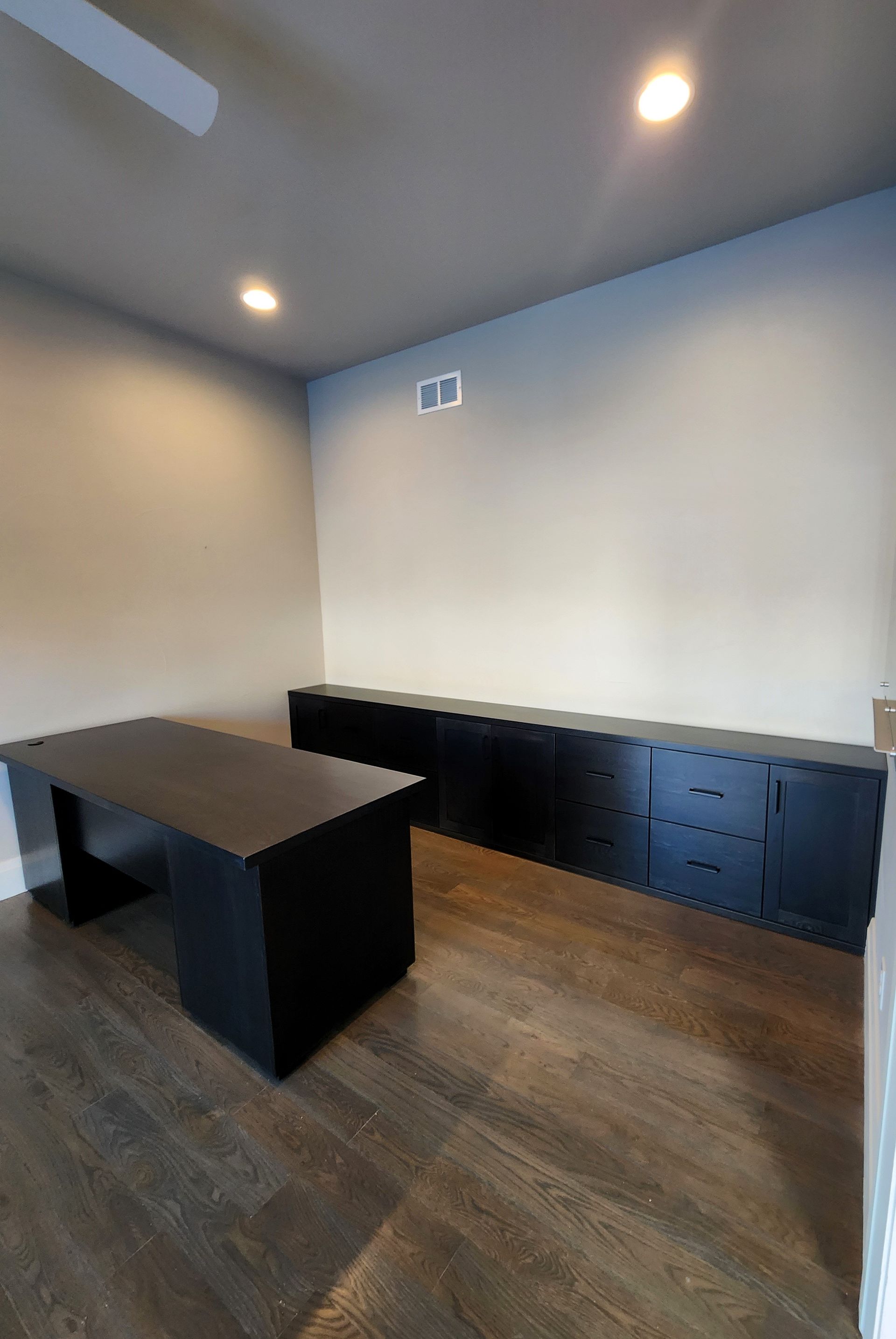 Office space with black desk and storage cabinets against light-colored walls; dark wood floor.