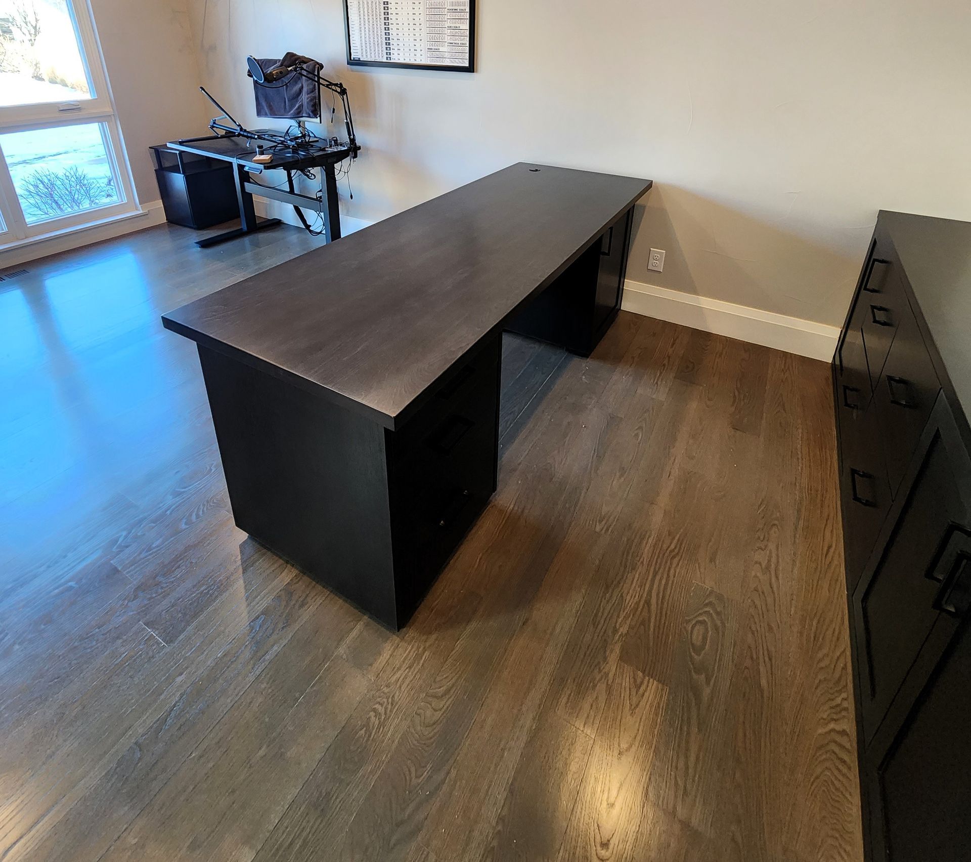 Dark wooden desk with black cabinets in a room with hardwood floors.