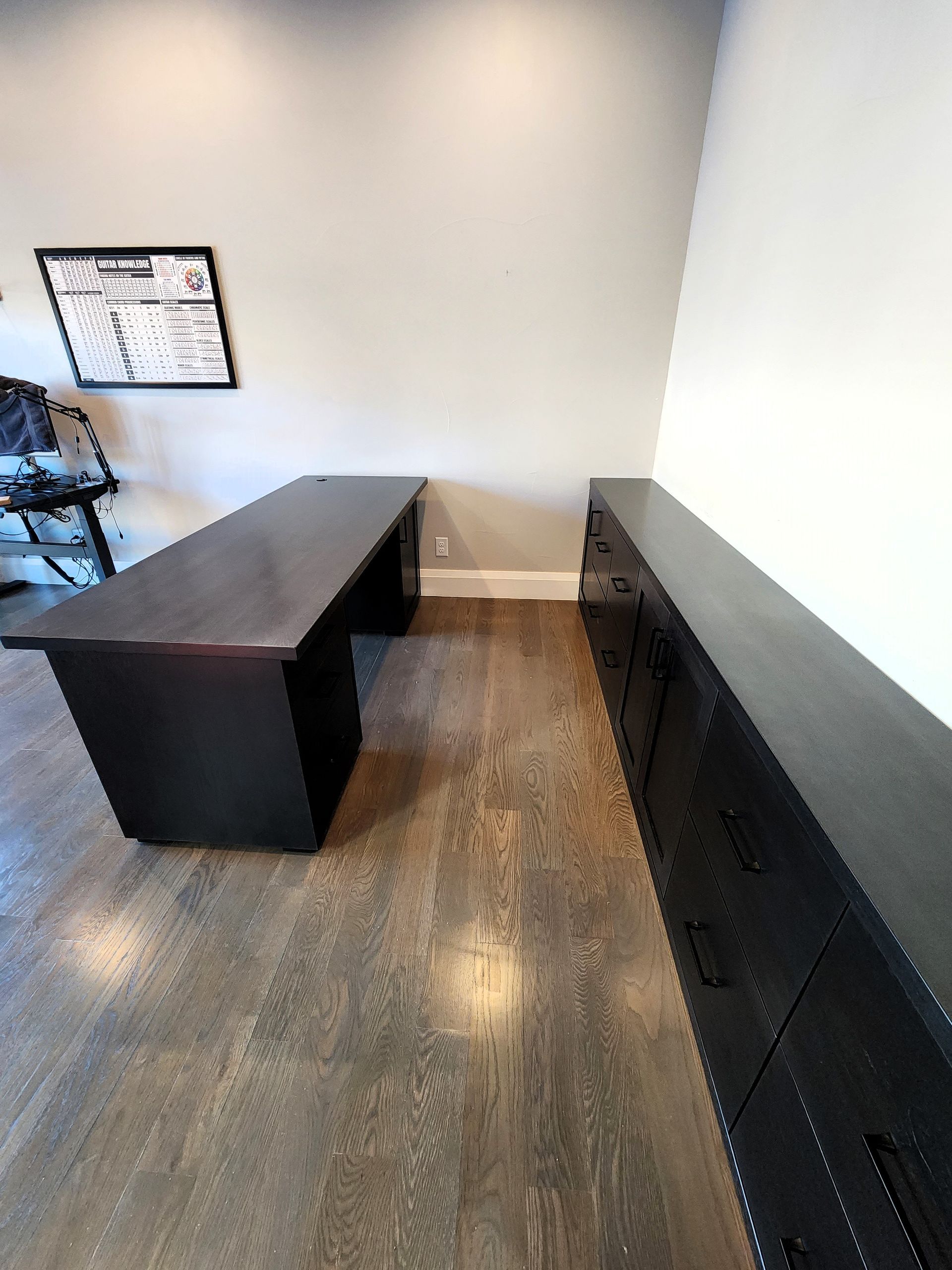 Dark wood desk and cabinet in office. Wooden floor, white walls.
