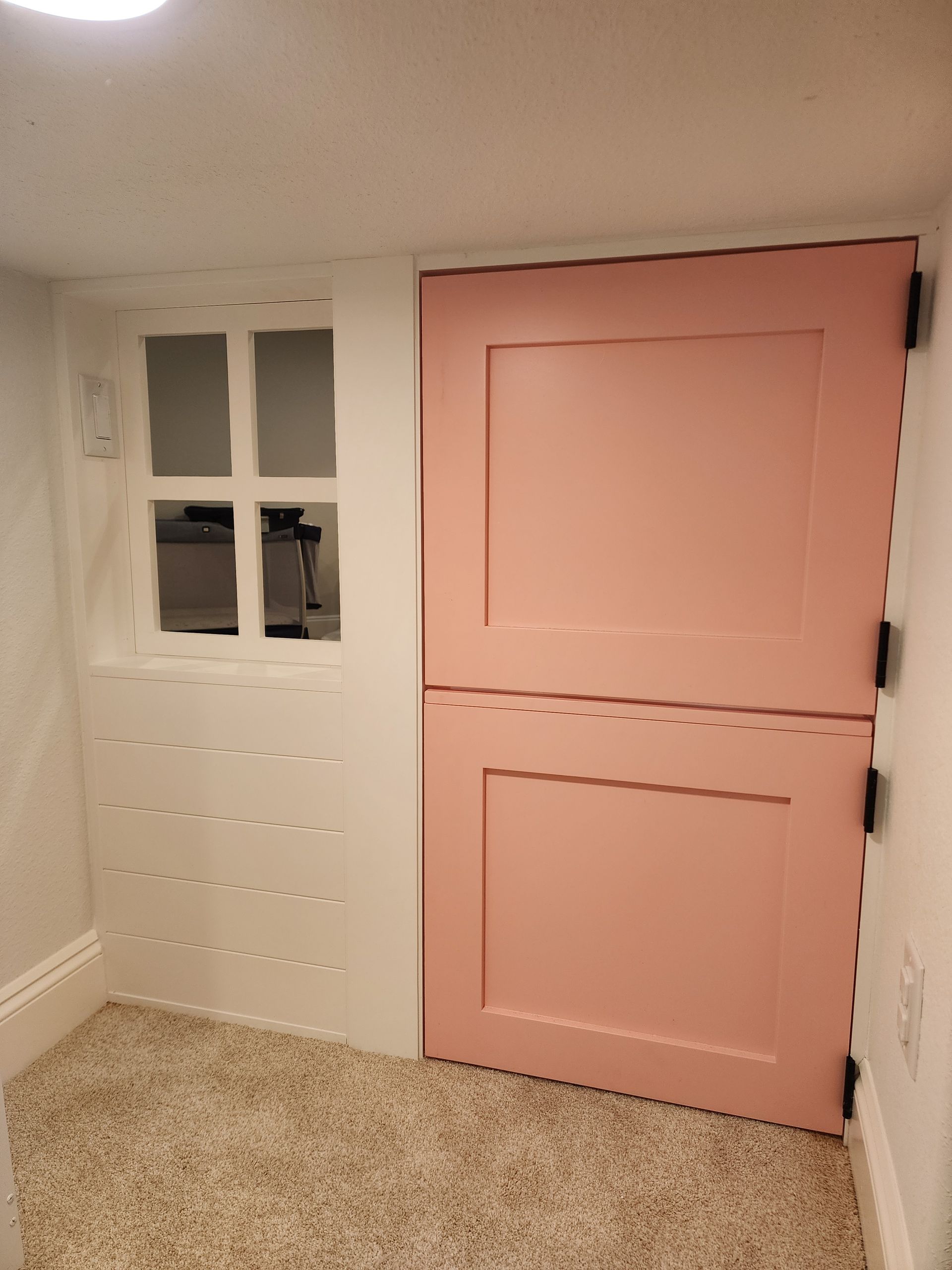 Pink, two-part Dutch door with white trim, next to a small window, in a room with beige carpet.