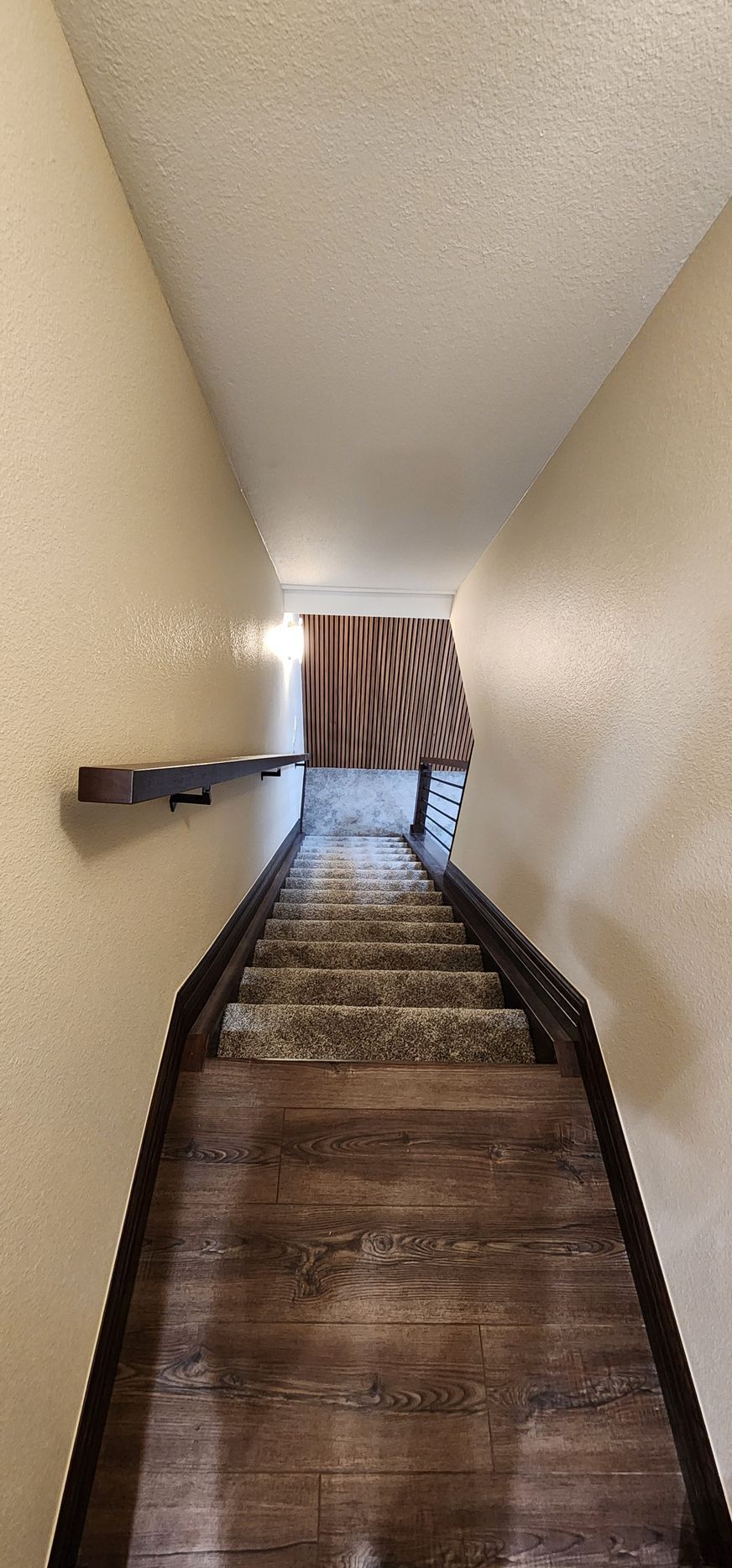 View of a staircase, descending into a room. Stair treads are wood, risers are carpeted. Handrail and walls are light colored.