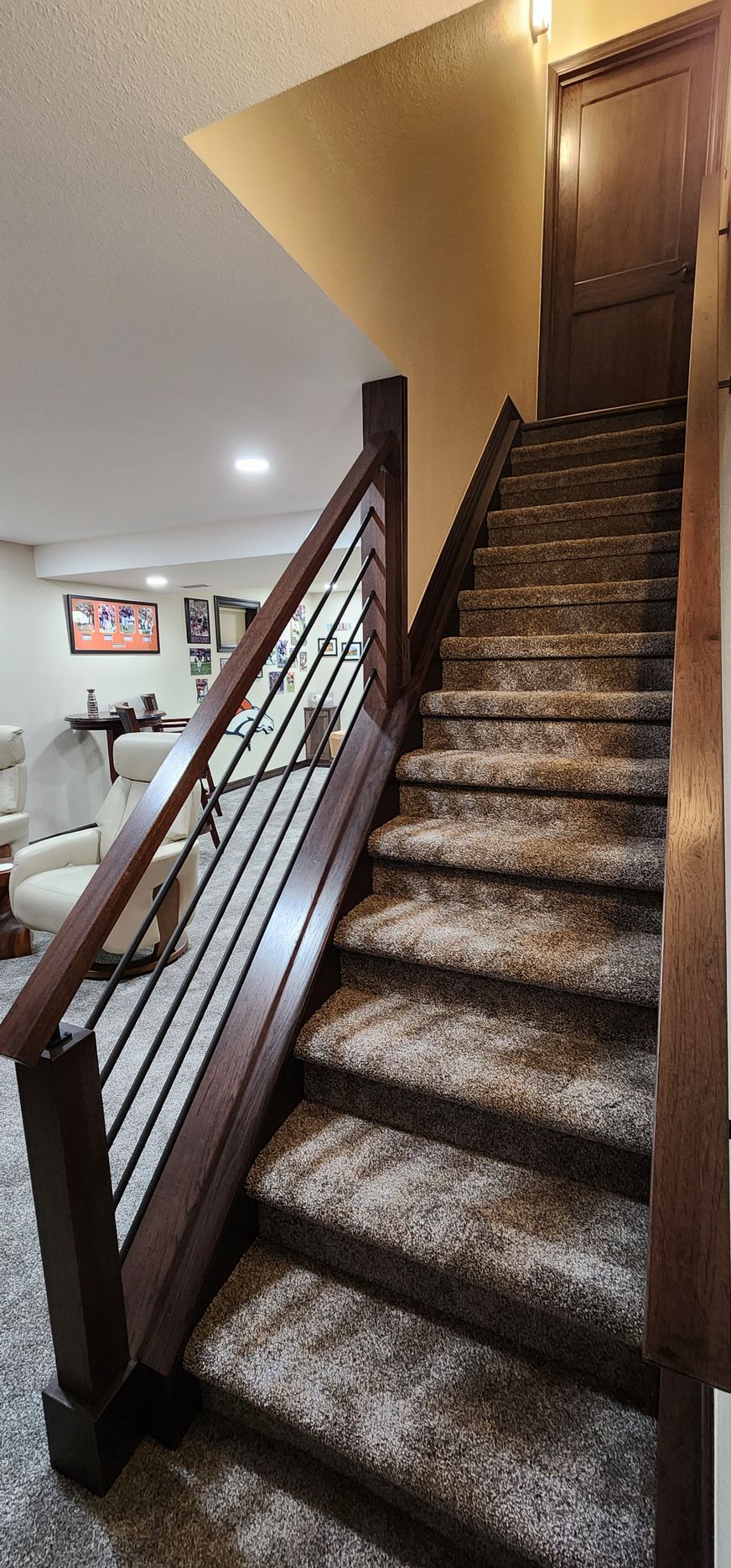 Staircase with carpeted steps, wooden handrail with black spindles, leading up to a closed door.