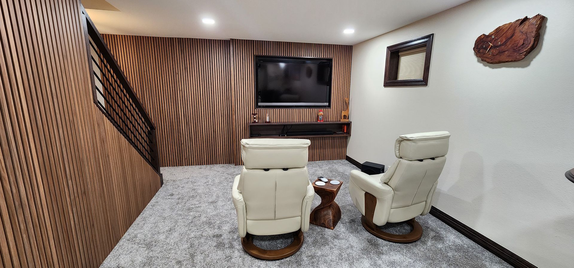 Cozy living space with TV, two cream swivel chairs, small table, wood accent walls, and gray carpet.