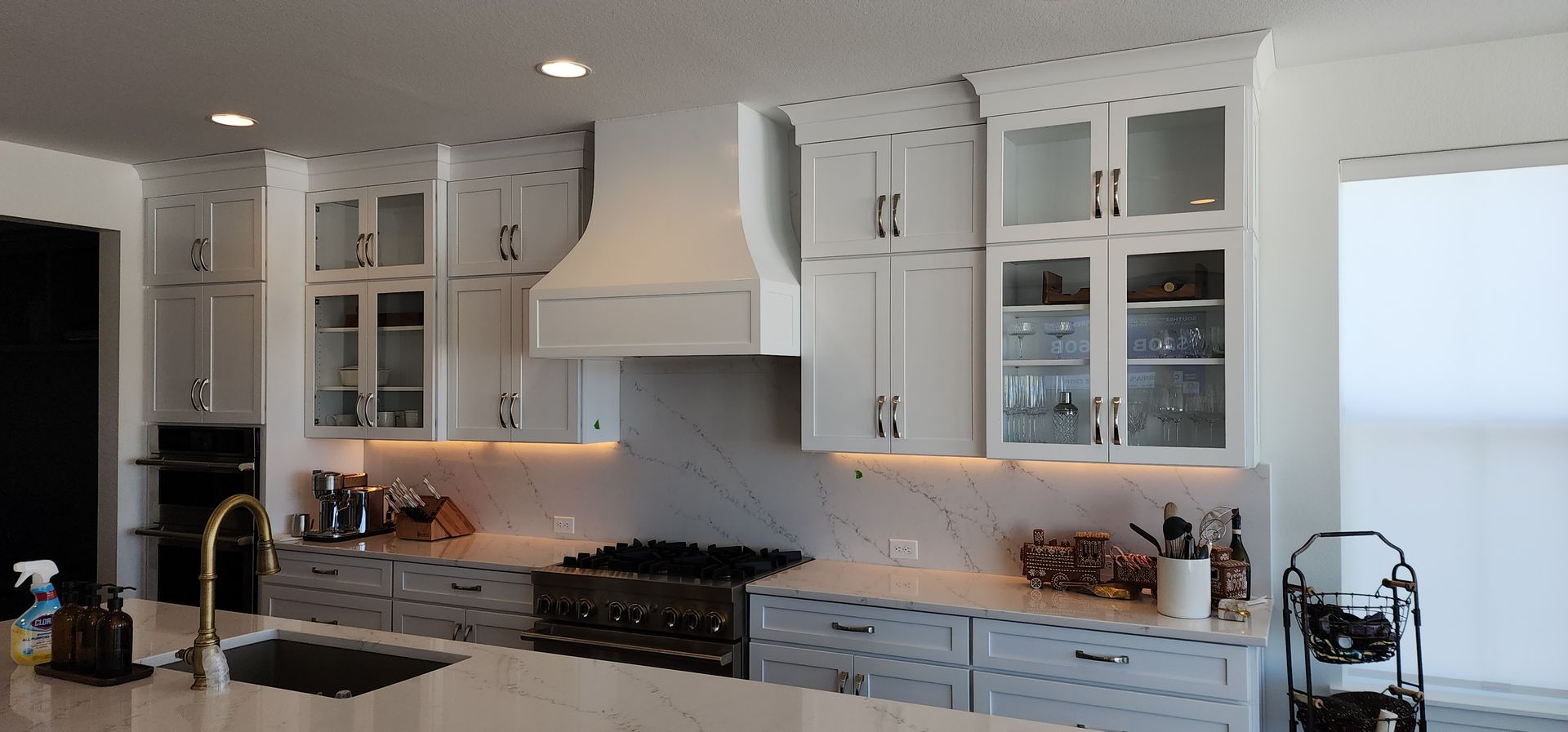 A bright, modern kitchen with white cabinets, a marble backsplash, and a gold faucet.