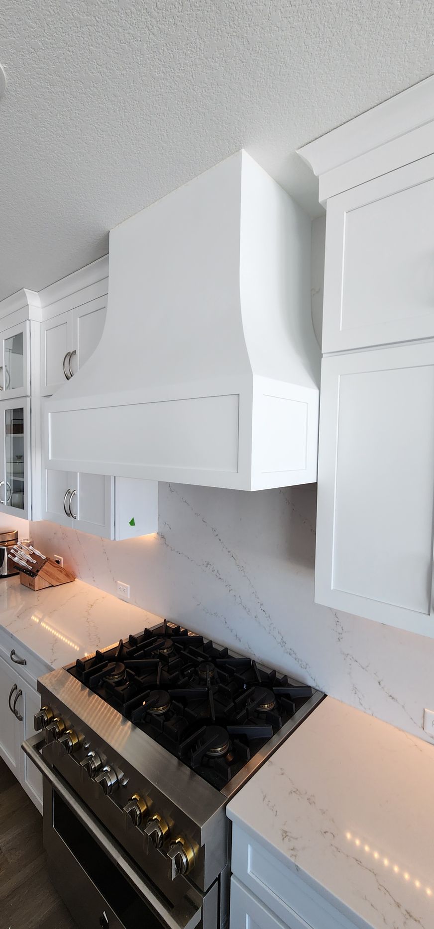 White kitchen range hood above a stainless steel stove on a white countertop.