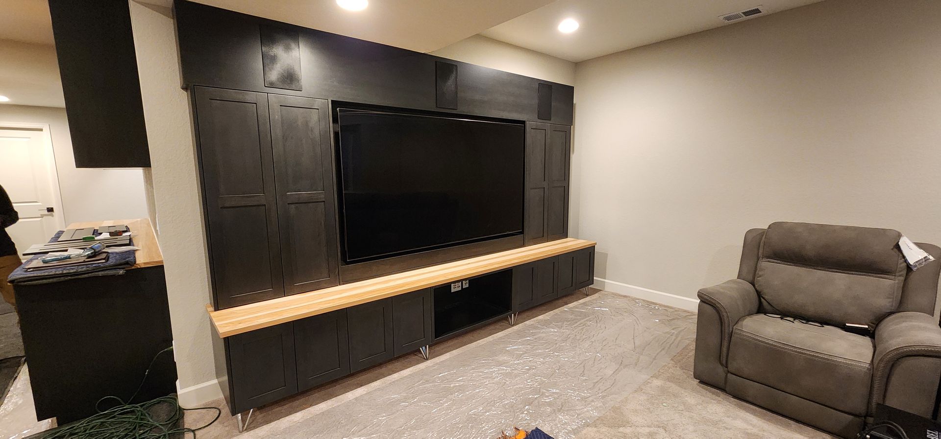 A black entertainment center with a large TV, wood trim, and a gray recliner in a room.