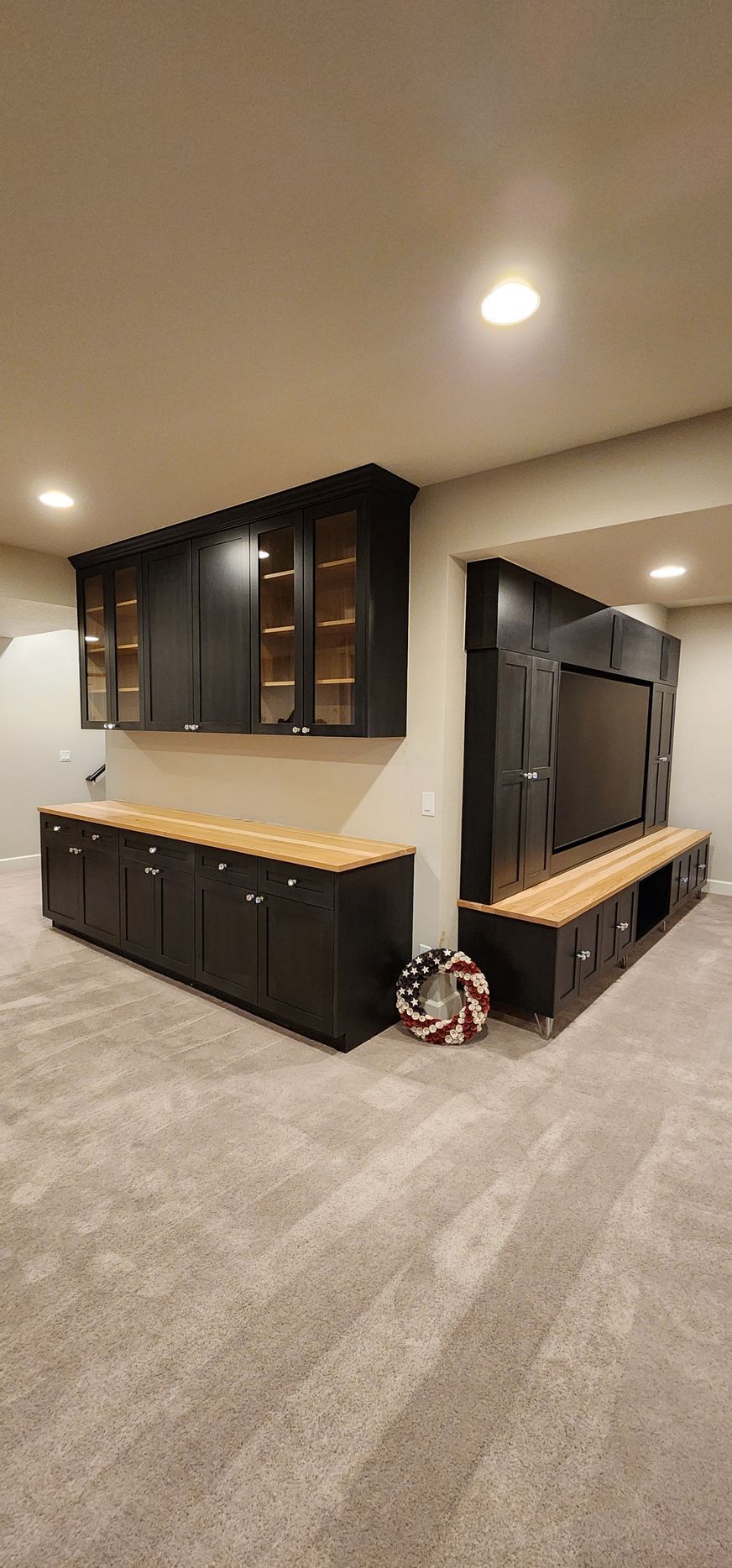 Basement entertainment center with black cabinets, light wood counters, and gray carpet.