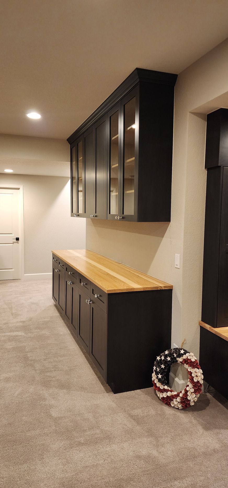 Dark cabinets with glass doors and a wooden countertop. A patriotic wreath sits on the carpeted floor.