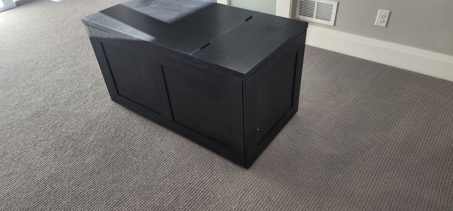 Black wooden box on a gray carpet. The box is rectangular and has a lid.