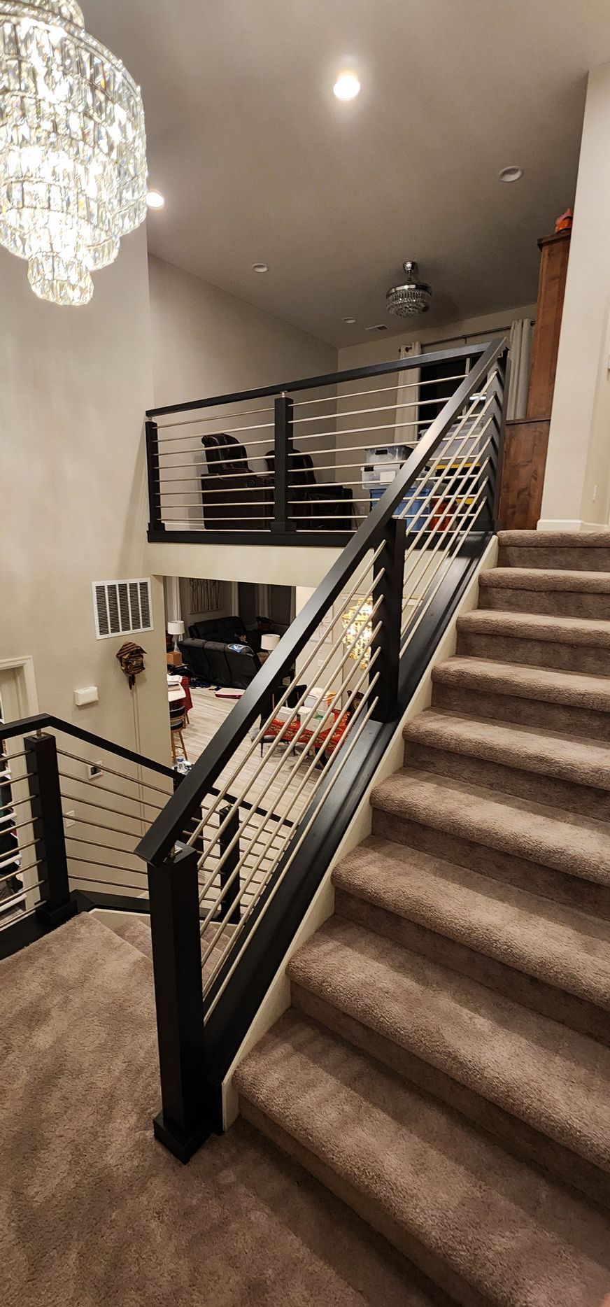 Staircase with black railing and cable wires, carpeted steps, and a chandelier in a home.