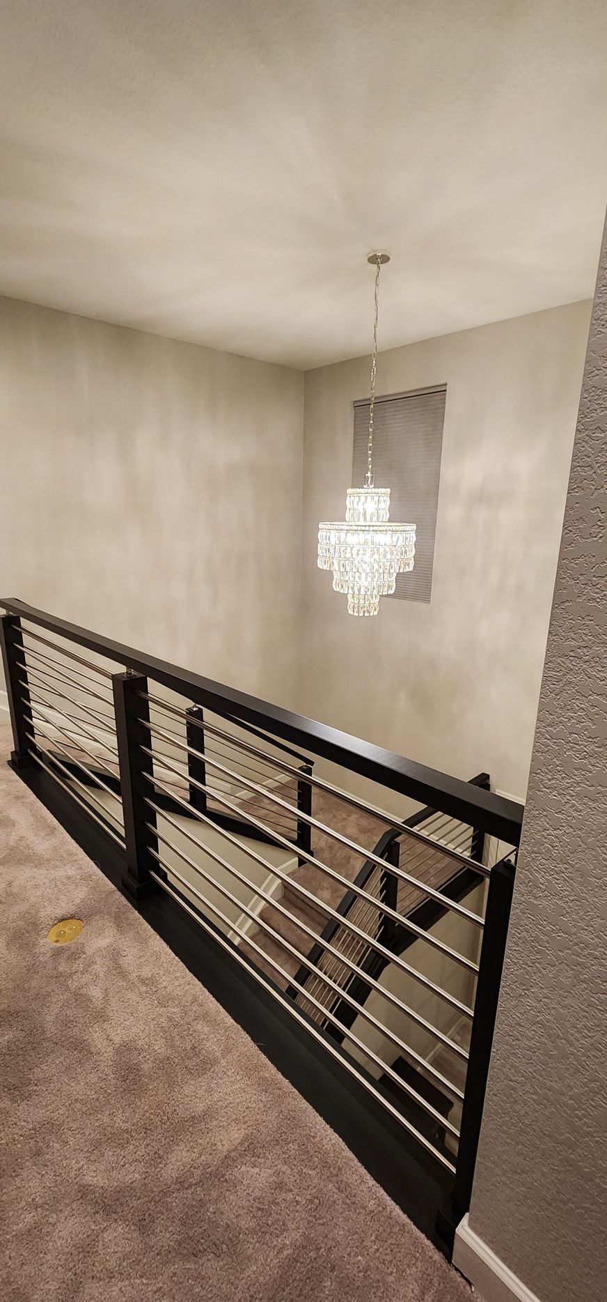 Staircase with black railing and horizontal metal rods. A chandelier hangs from the ceiling.