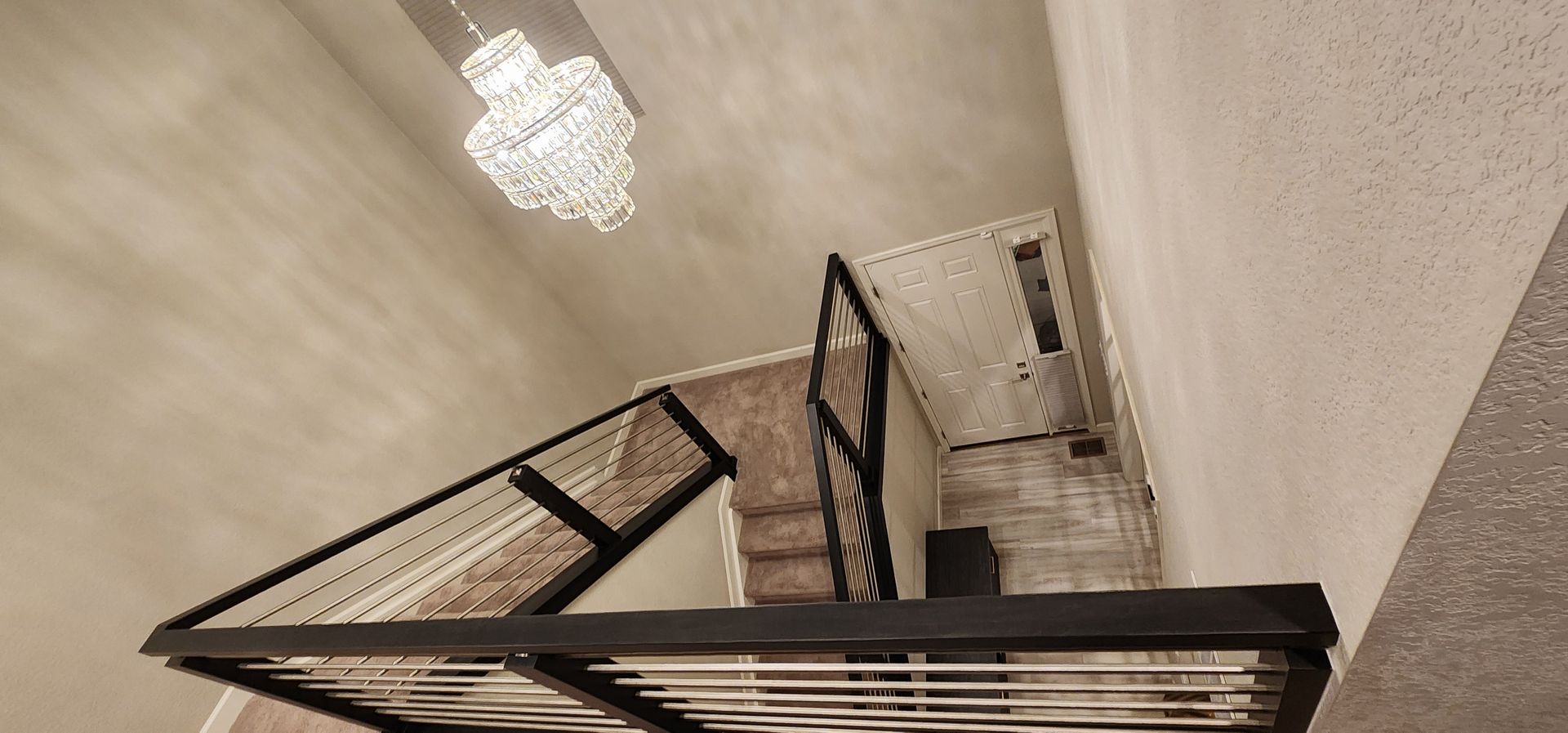 Staircase with black railing and chandelier overhead.