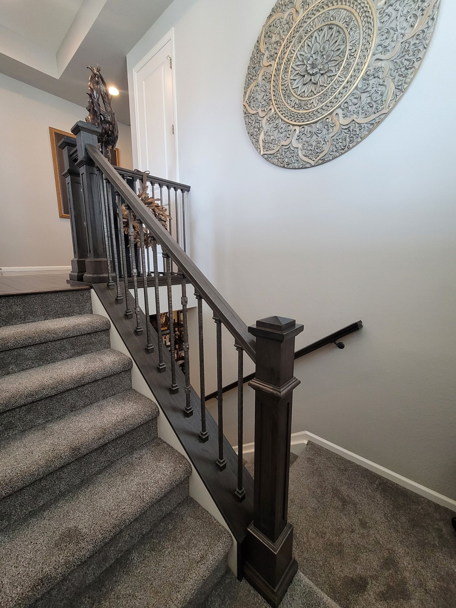 Staircase with gray carpet steps, dark brown banister, and decorative wall art.