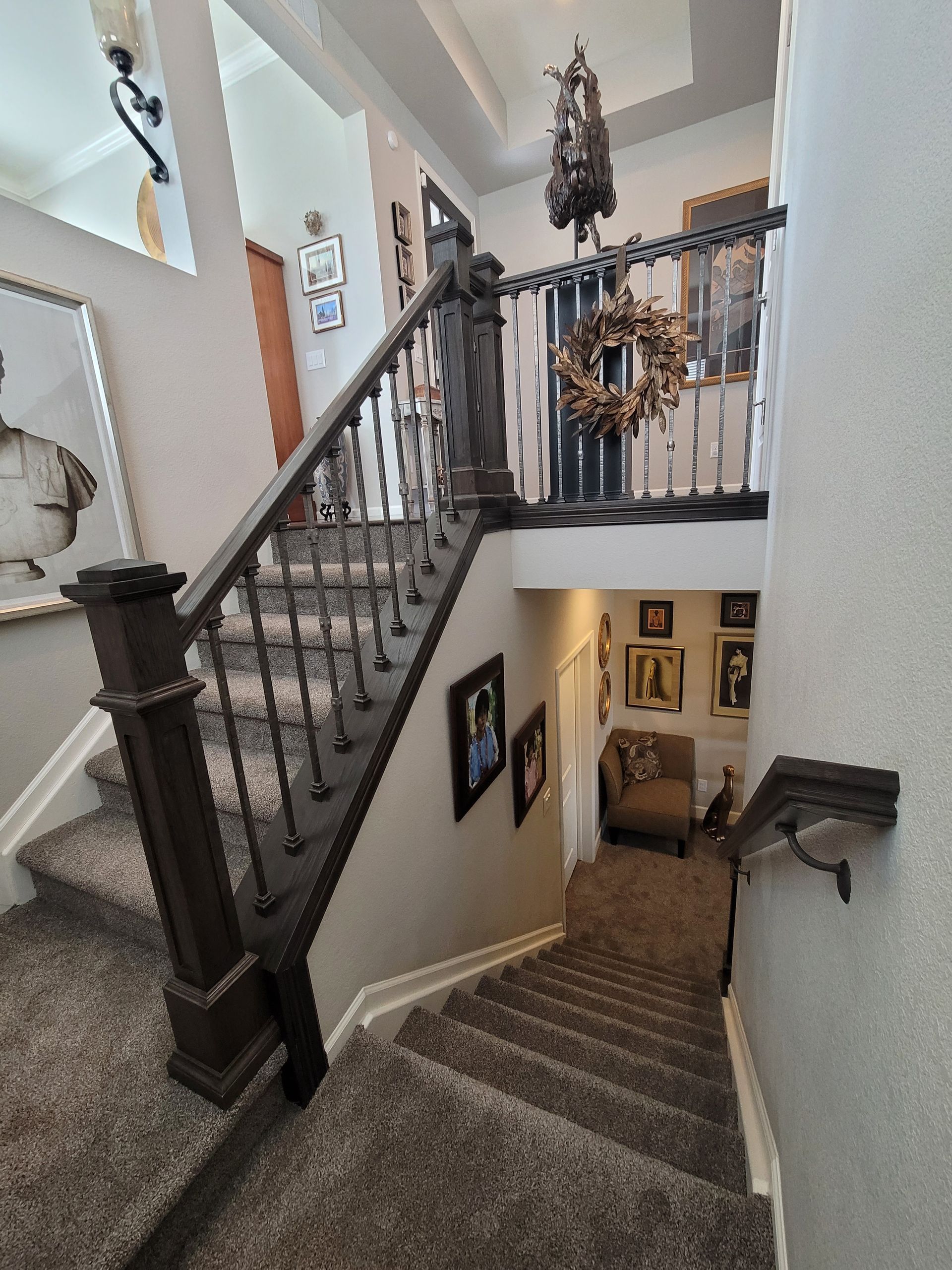 Staircase with dark wood banister and carpeted steps, leading down to a hallway with framed pictures.