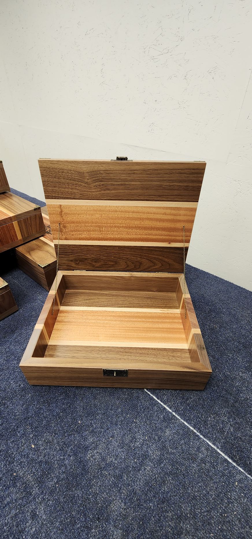 Wooden box, open, with variations of brown and tan wood, on a blue fabric surface.