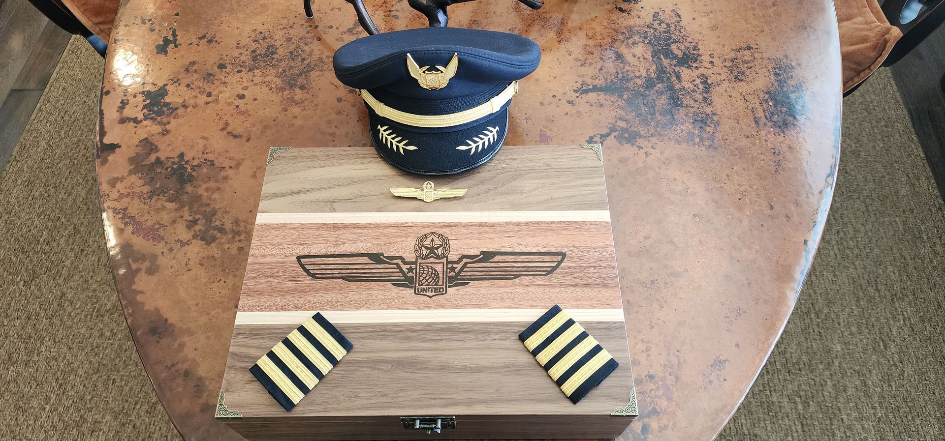 Pilot hat, box with wings emblem, and insignia on a patterned brown surface.