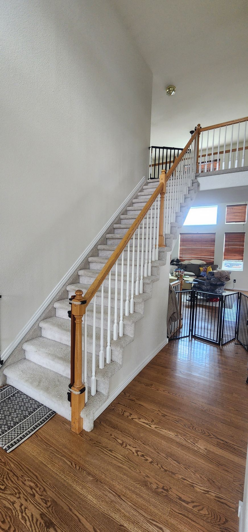 Wooden staircase with white spindles and light carpet. Dark hardwood floor and high ceiling.