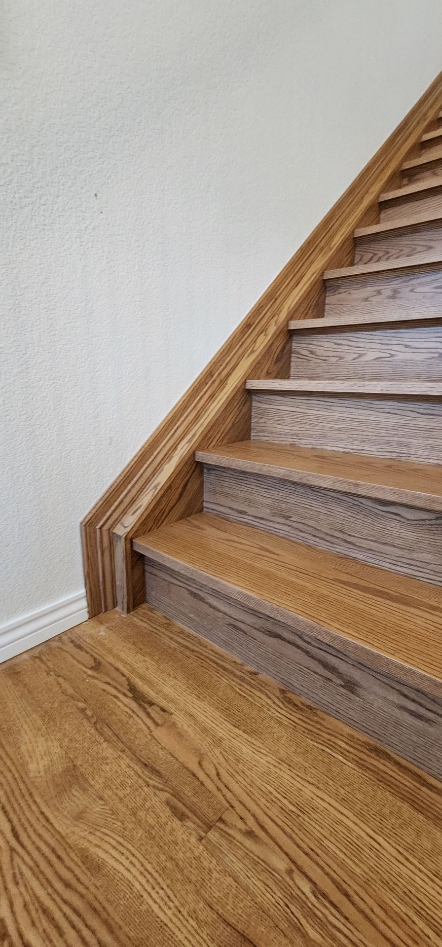 Wooden stairs with matching flooring and banister against a white wall.