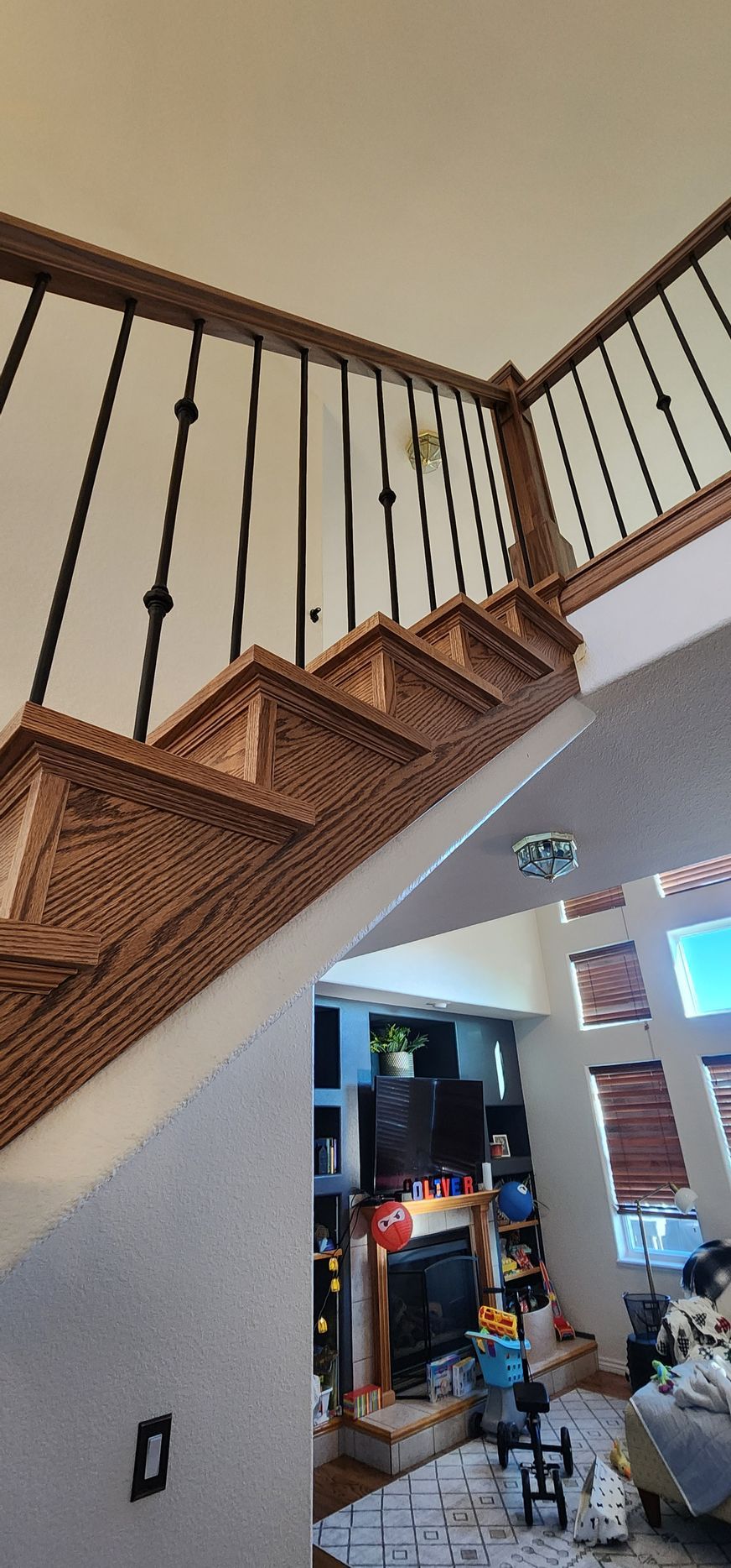 Wooden staircase with black railings, leading upwards. The bottom of the stairs reveals a living area.