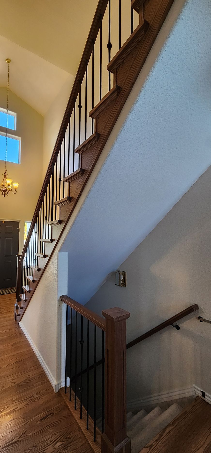 Staircase with wood steps and railing, leading up to a tall, light-colored ceiling.