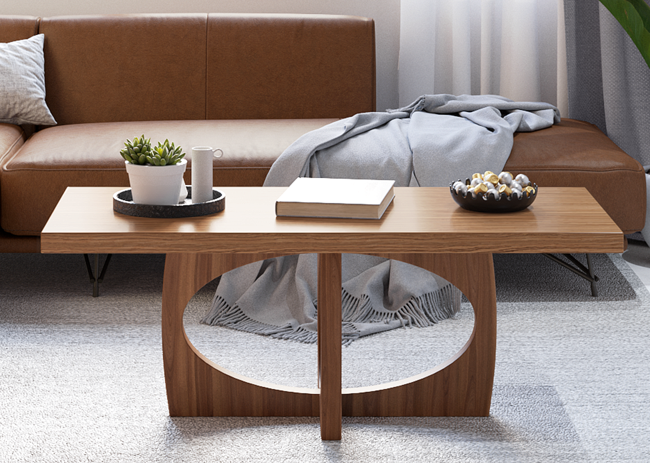 Wooden coffee table in front of a brown leather couch with a blanket, plant, book, and decorative bowl.
