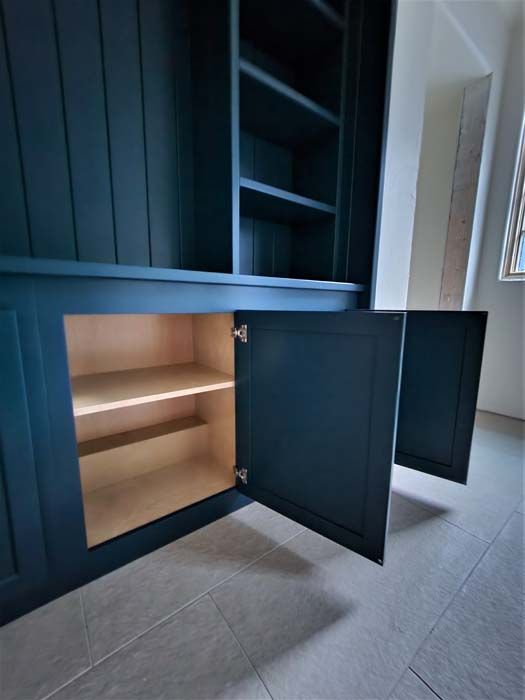 Dark blue built-in cabinet with open doors, revealing light wood shelves. Beige walls and gray floor.