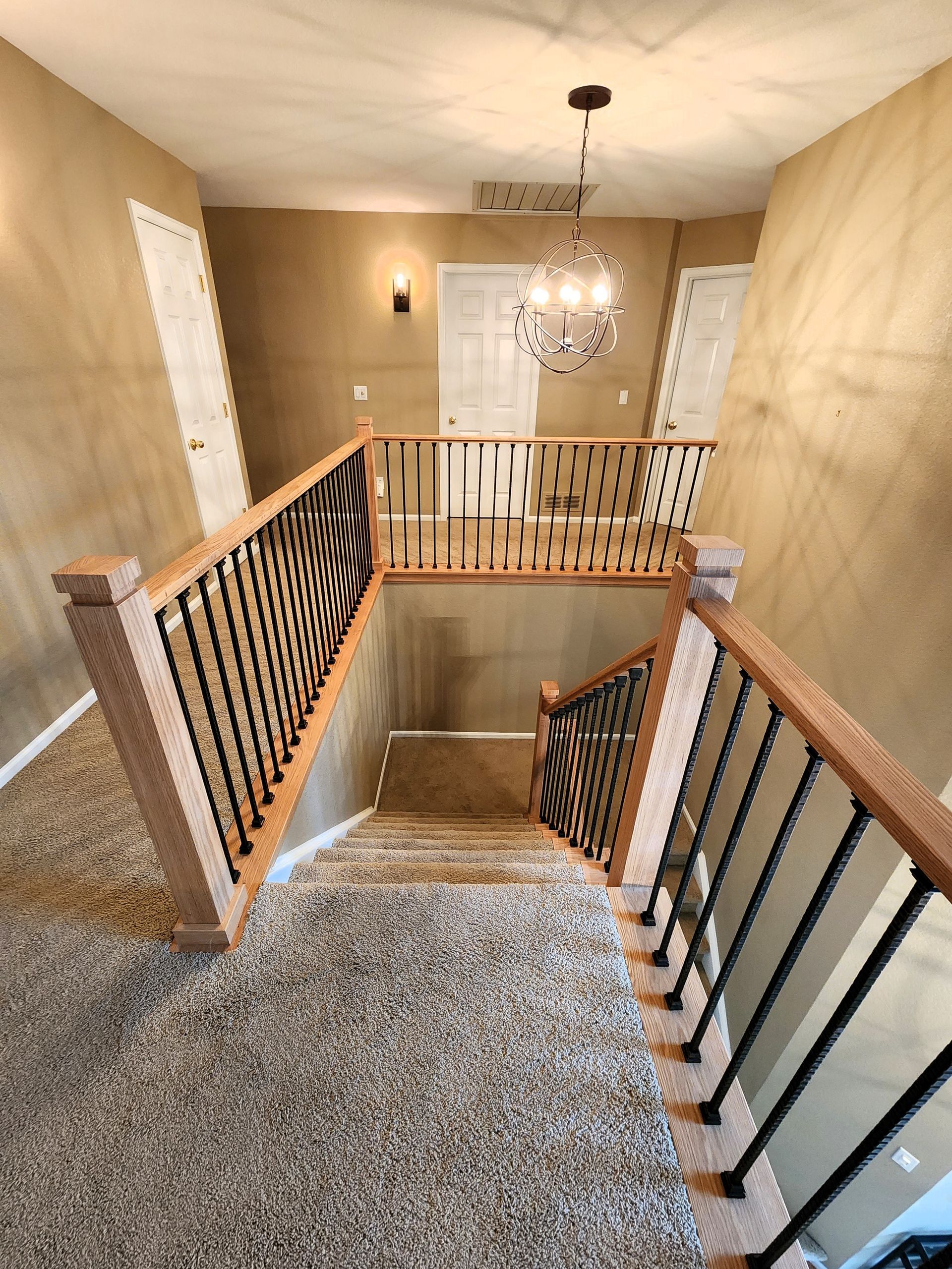 Staircase with brown wooden railing and black iron spindles. Tan walls and a carpeted floor.
