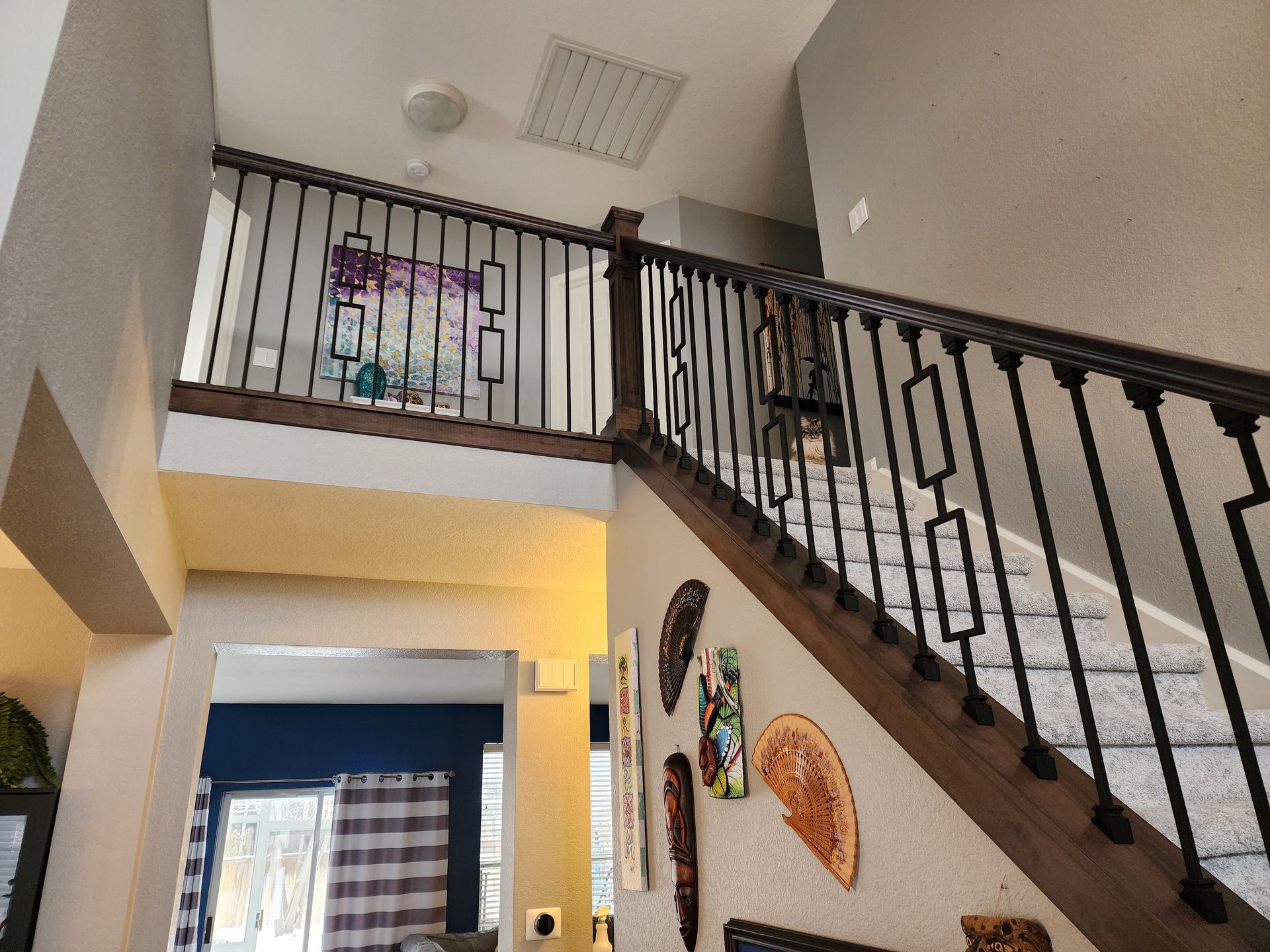 Staircase with wooden handrails and black metal balusters. Decorative wall art and a view into another room.