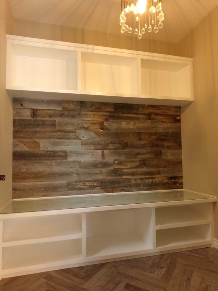 Built-in white shelves above and below a rustic wood wall, with a hanging chandelier in the ceiling.