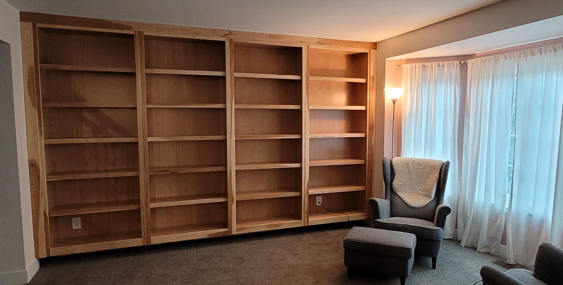 Built-in wooden bookshelves along a wall, with a reading chair and window to the right.