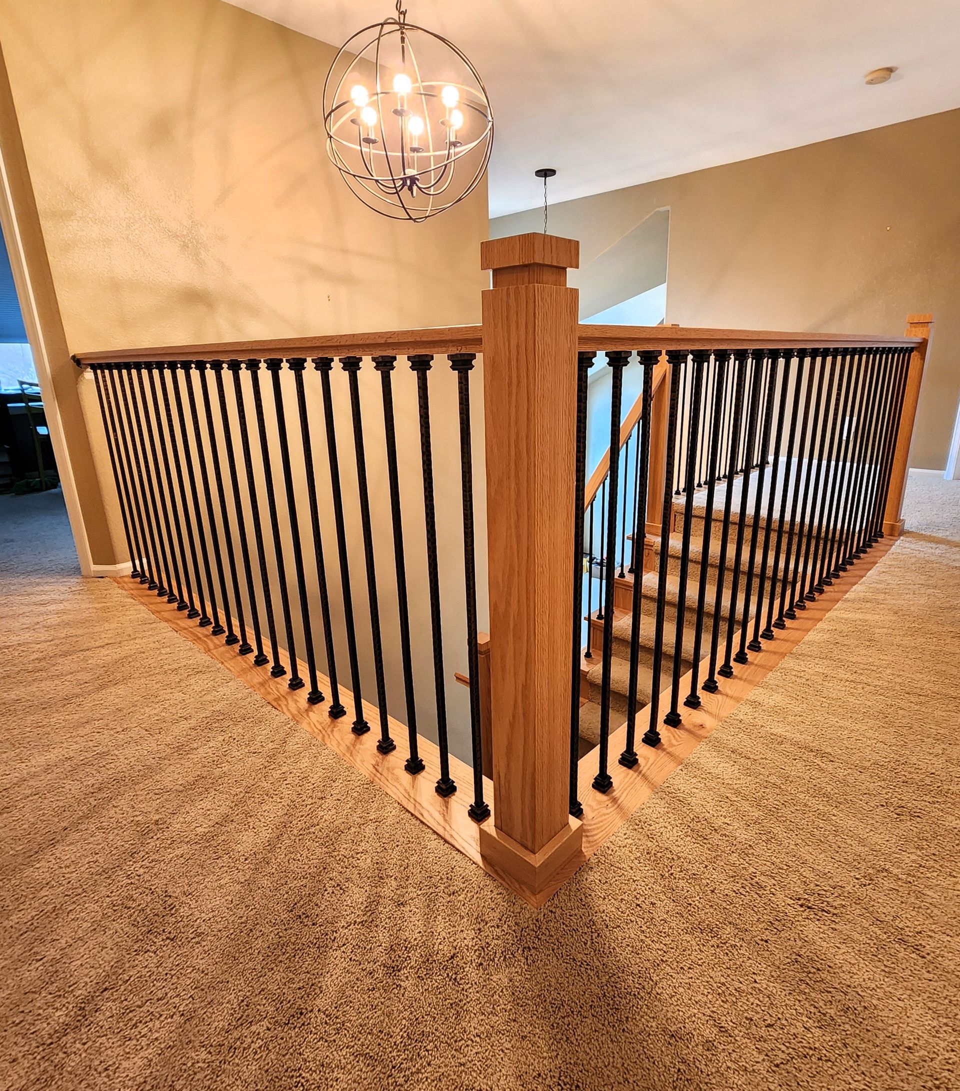 Staircase with wooden railing and black balusters, carpeted floor, and chandelier overhead.