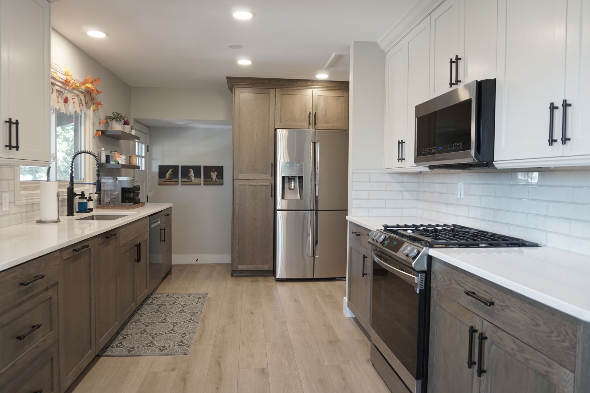 Modern kitchen with gray and white cabinets, stainless steel appliances, and wood floors.