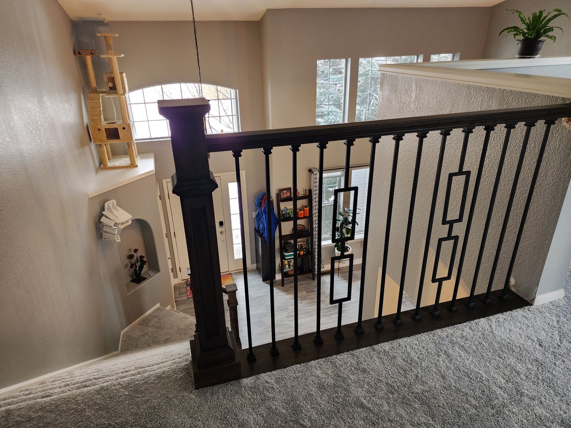 View from a second story staircase, looking down at a hallway with a decorative black railing and a cat tree.