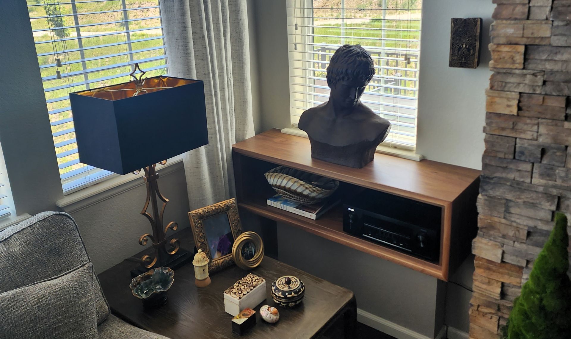 Living room corner with lamp, console table with bust, and stone accent wall.