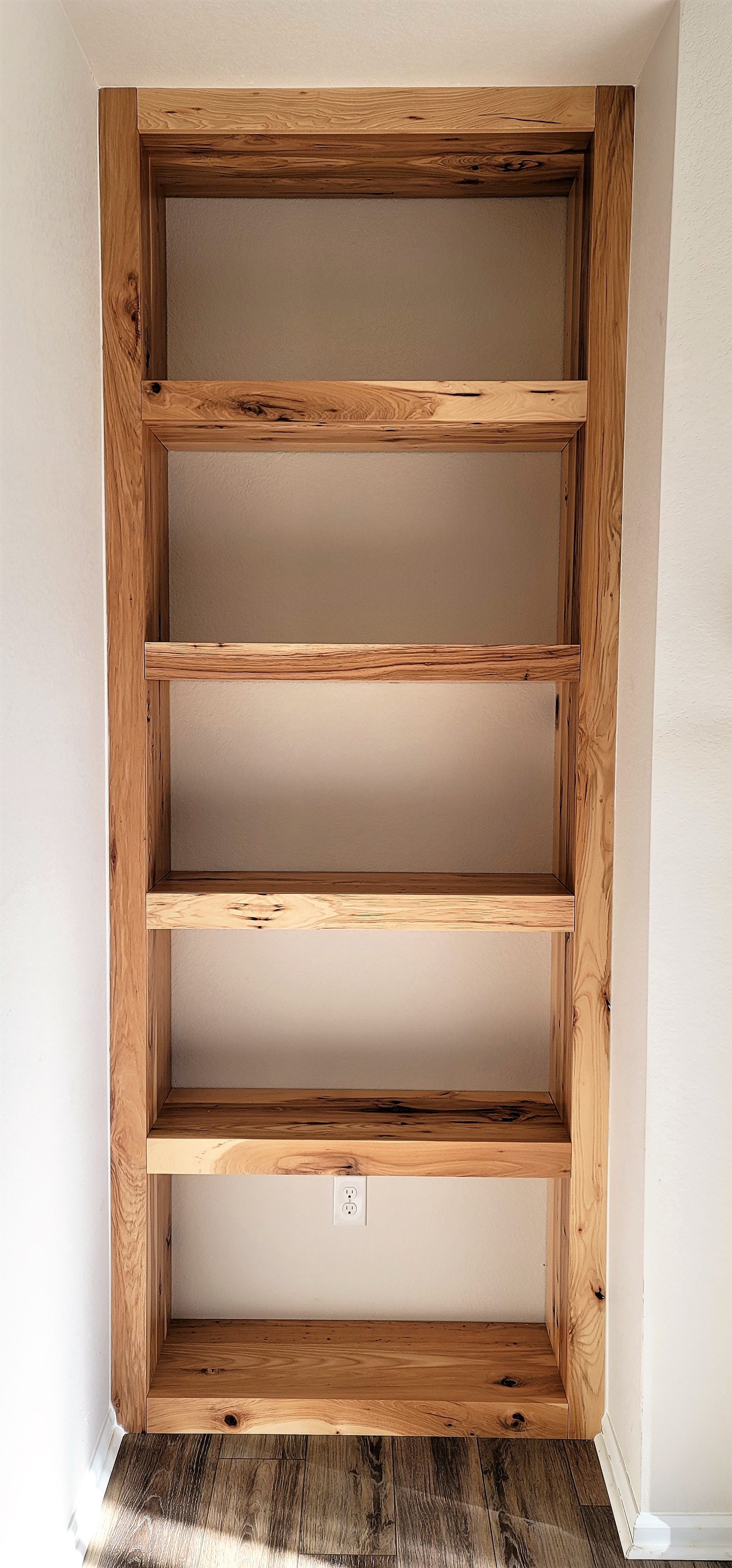 Wooden built-in shelving unit with five shelves, mounted on a neutral wall.