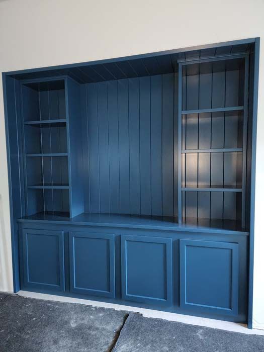 Built-in, dark blue bookcase with shelves and cabinets. Recessed into a white wall.