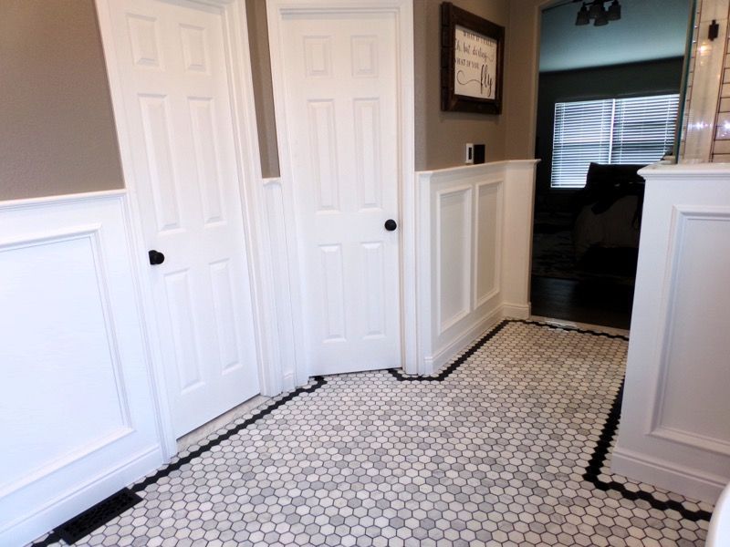 Bathroom with white wainscoting, two doors, and a tiled floor with black and white penny tiles.